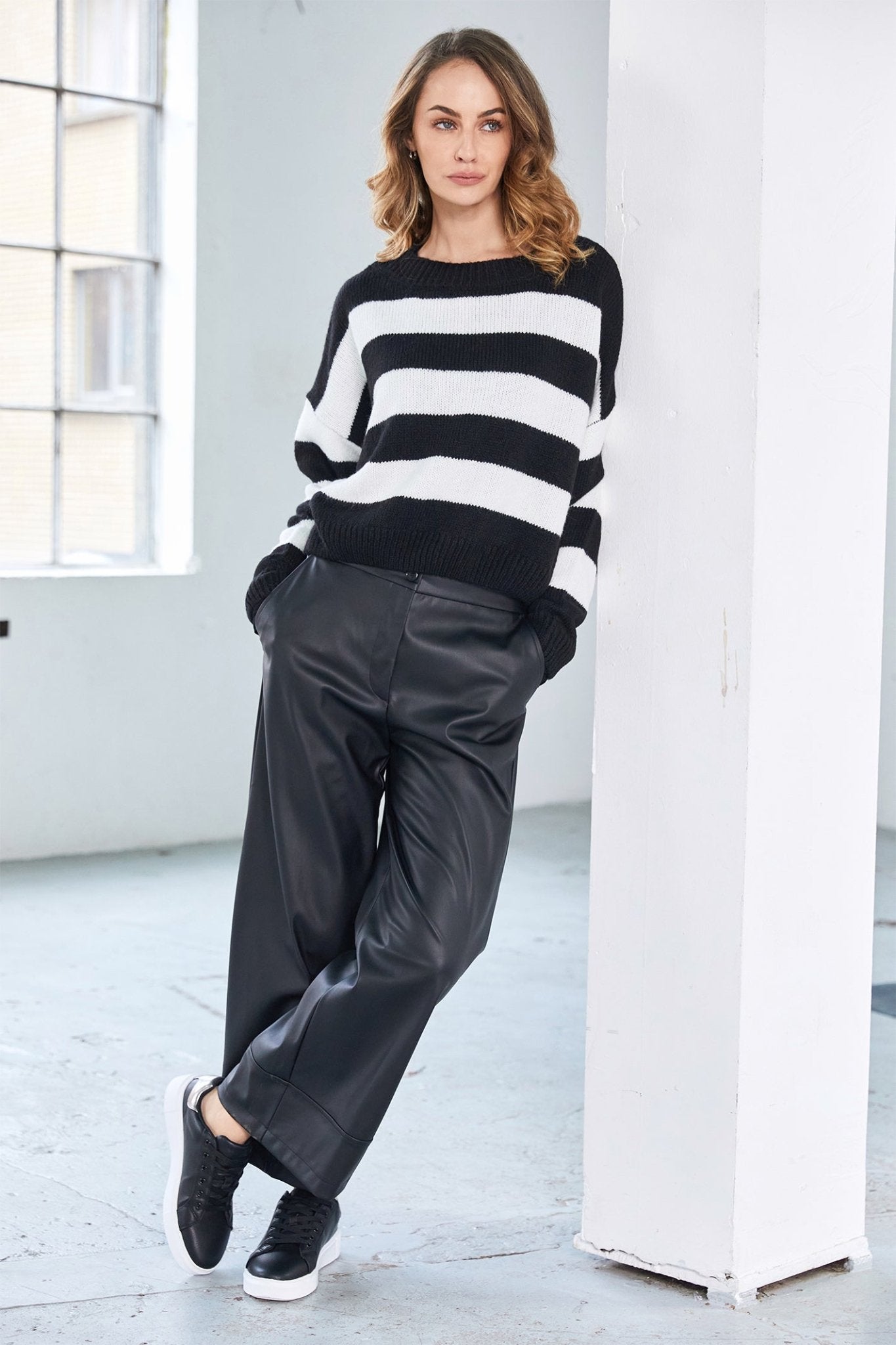 Woman wearing a black and white striped sweater and black pants in a minimalistic setting.