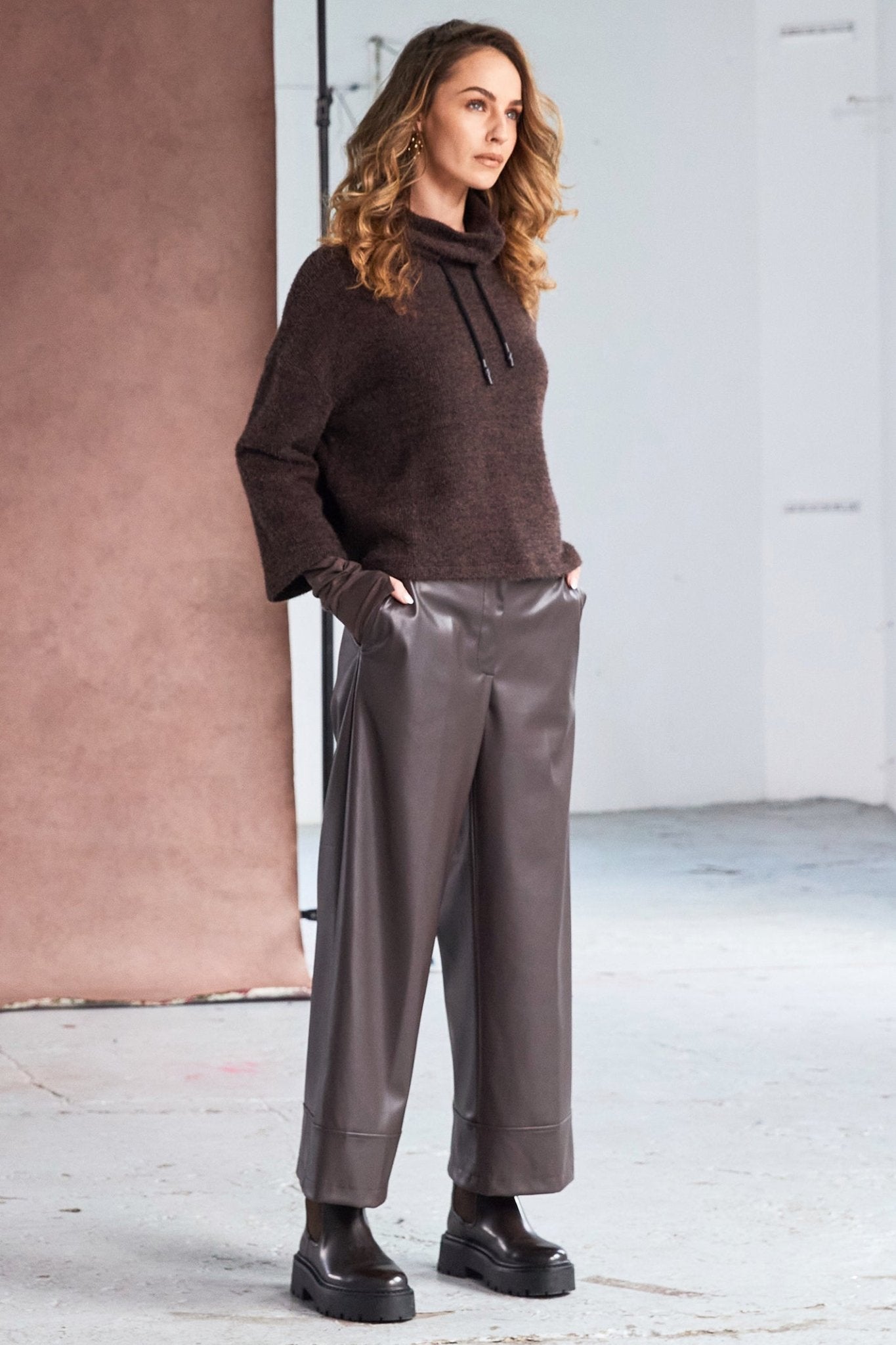 Woman wearing a brown sweater and faux leather pants in a minimalistic setting