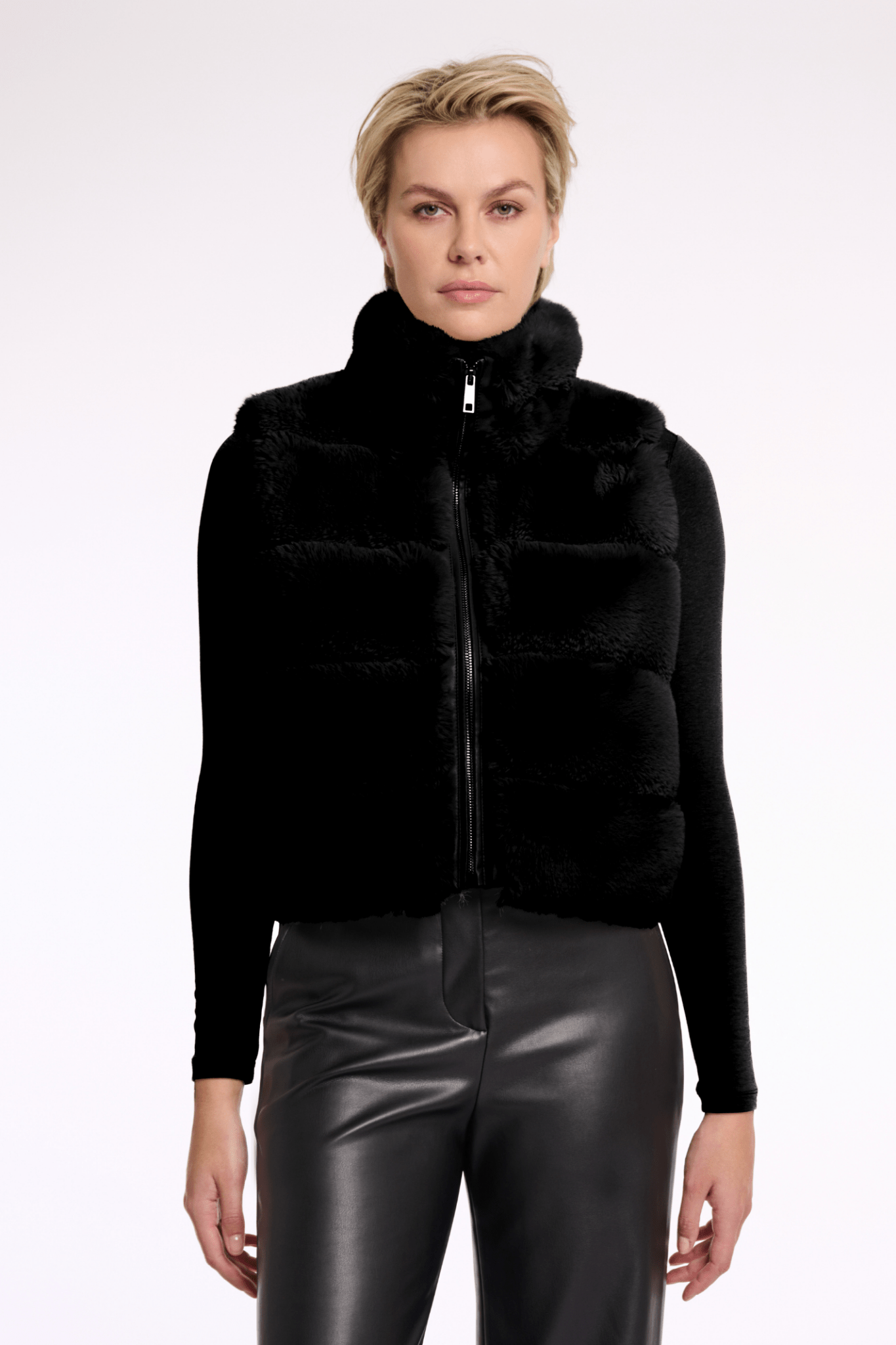 Woman wearing a black puffer vest over a black top with leather pants on a white background