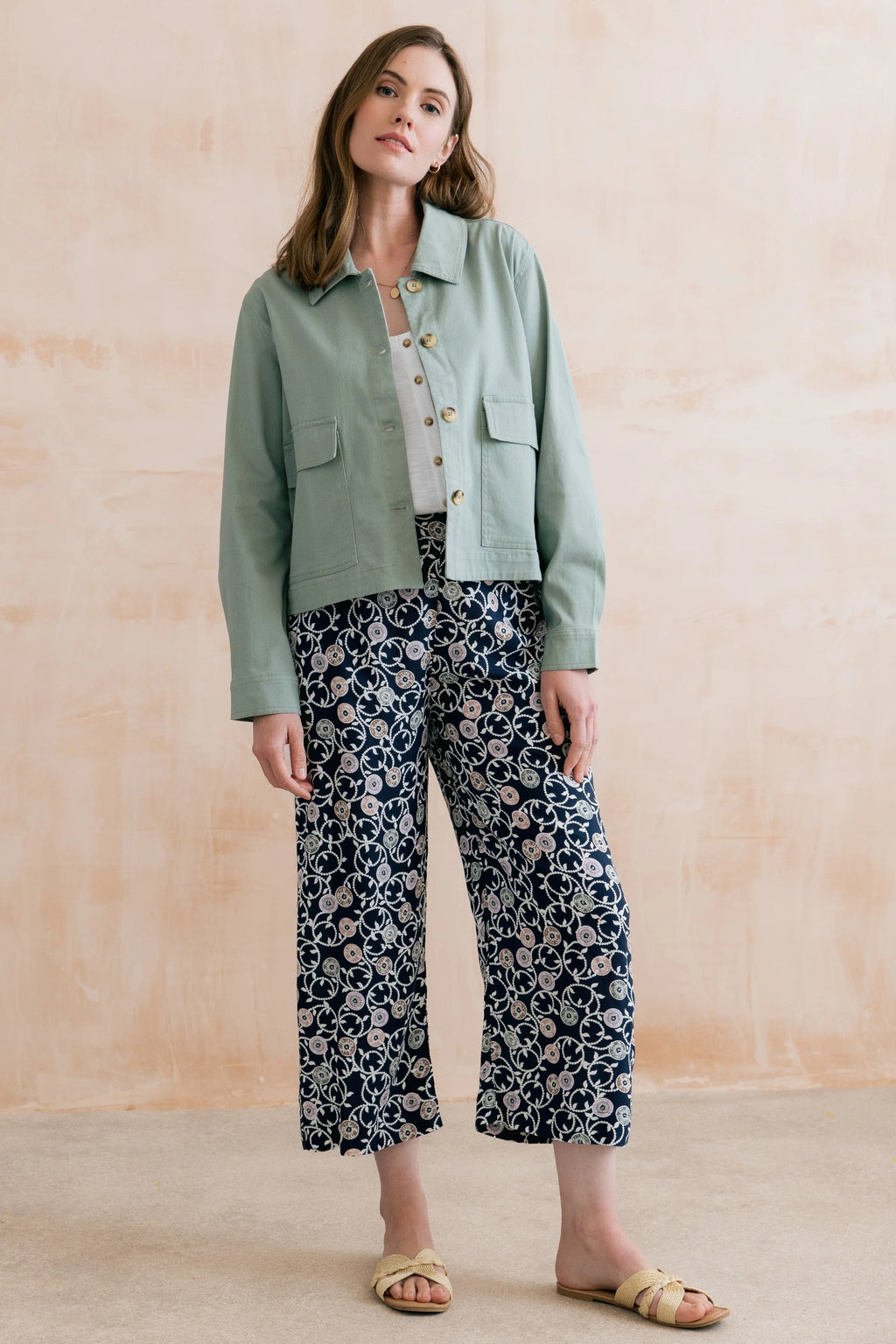 Model wearing Lily & Me LM26023 Greta Trousers Sea Holly Navy with floral pattern paired with a light green jacket by Lily & me. Shop Lily & me at Dotique.