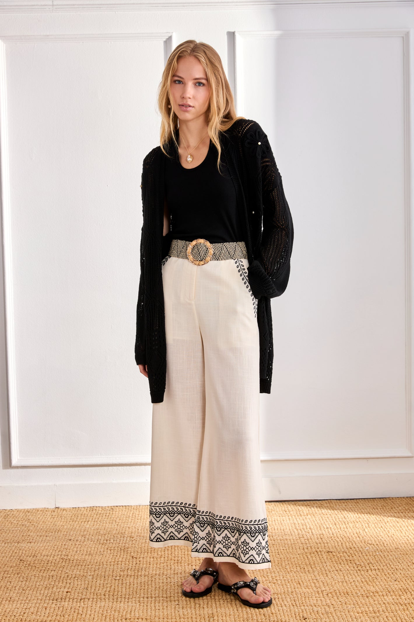 Model standing in black top and cardigan wearing NKN Nekane Arsi Ivory Linen Trousers with Embroidery on Hem and Pocket by nkn nekane, shop Dotique