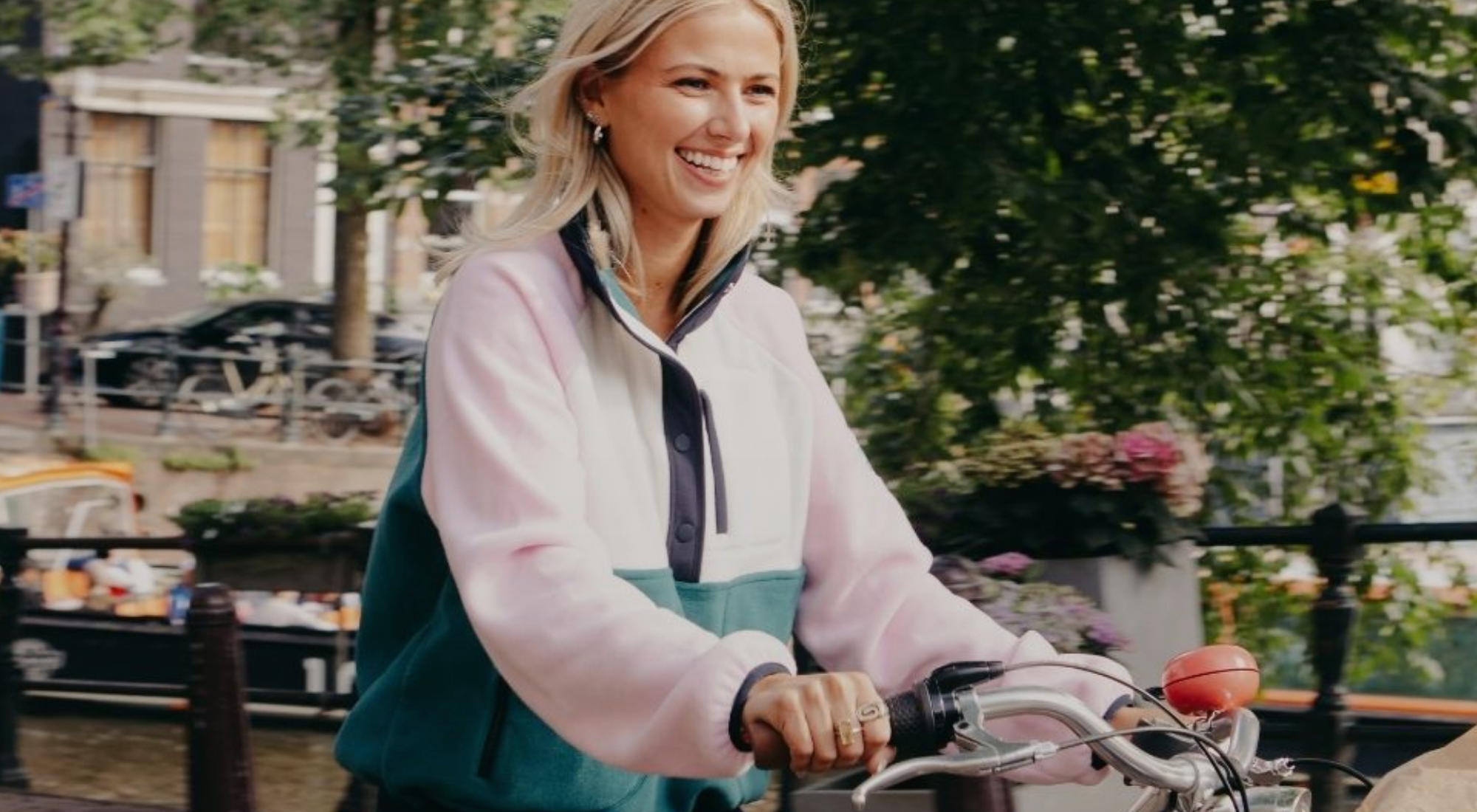 Woman riding a bicycle in an urban setting with buildings and trees in the background