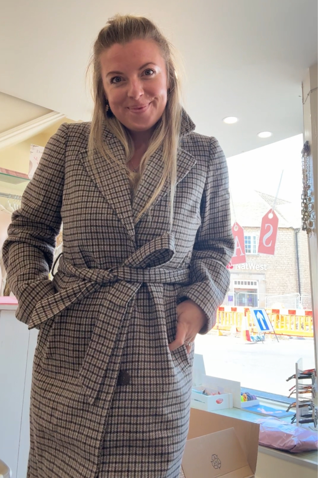 Woman wearing the Numph 707347 Nuelana Coat Black Coffee with a belted waist and checkered pattern, shop Numph at Dotique.