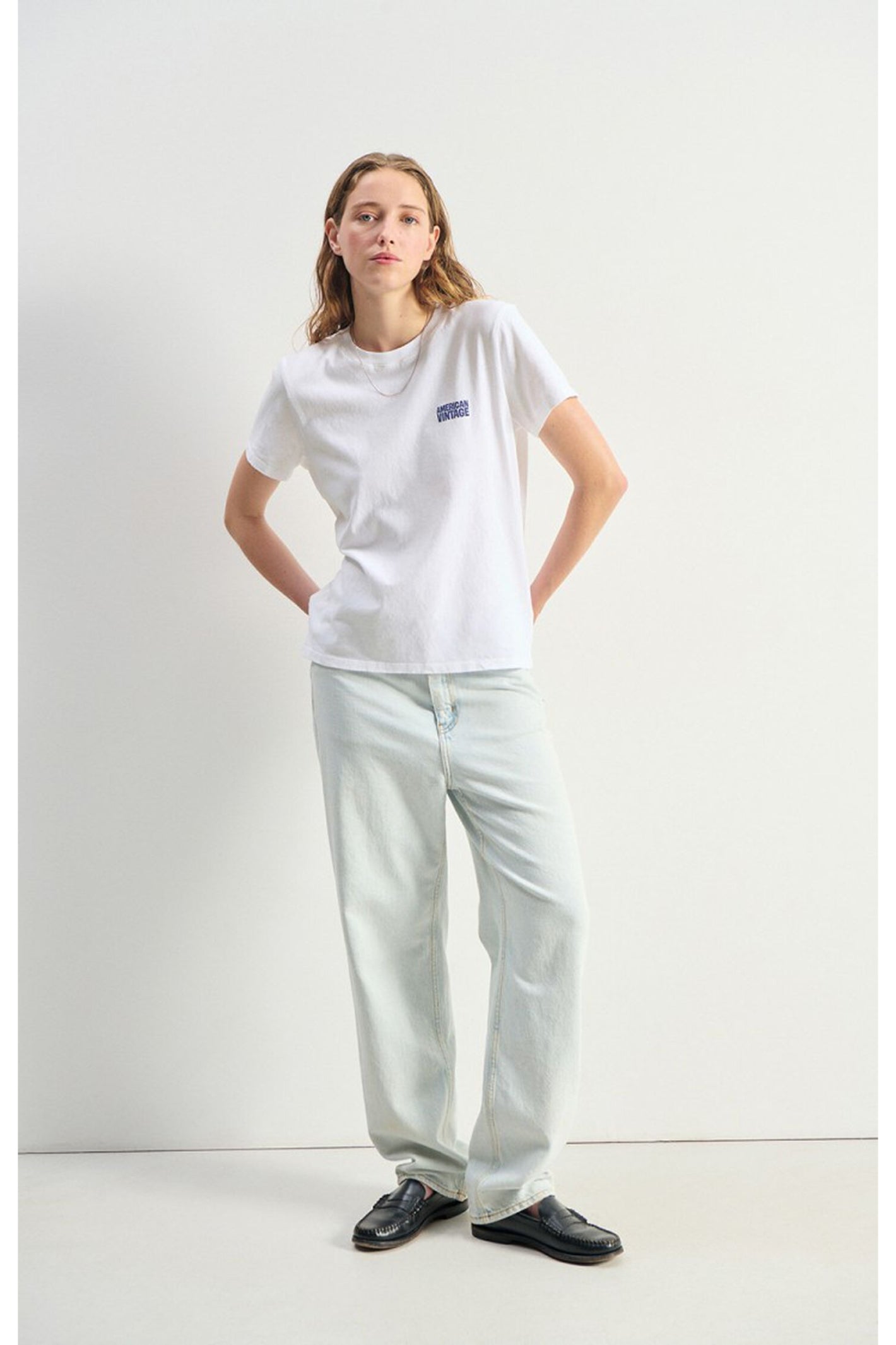 Model wearing American Vintage Ykobow Cotton T-Shirt – Blanc with light denim jeans and black loafers in a minimalist studio, shop American Vintage at Dotique.