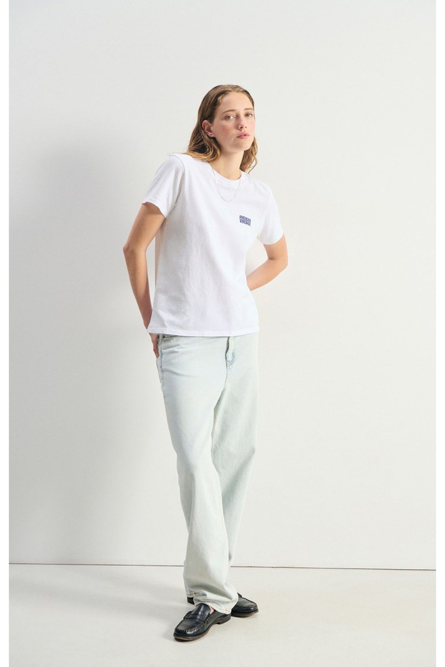 Model wearing a white American Vintage Ykobow Cotton T-Shirt – Blanc paired with light jeans and black shoes, shop American Vintage at Dotique.