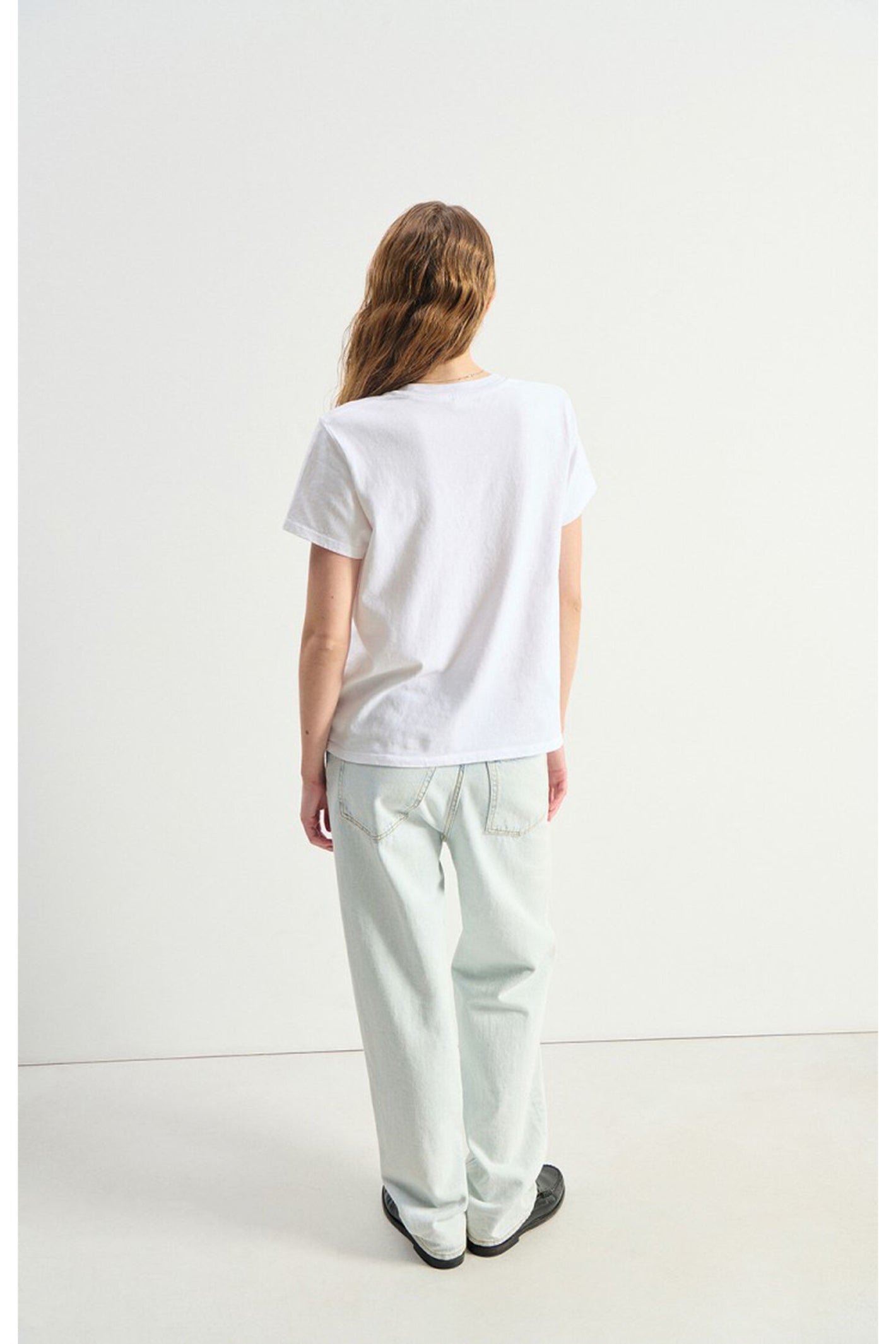 Model wearing a plain white American Vintage Ykobow Cotton T-Shirt – Blanc paired with light washed jeans and black shoes, shop American Vintage at Dotique.