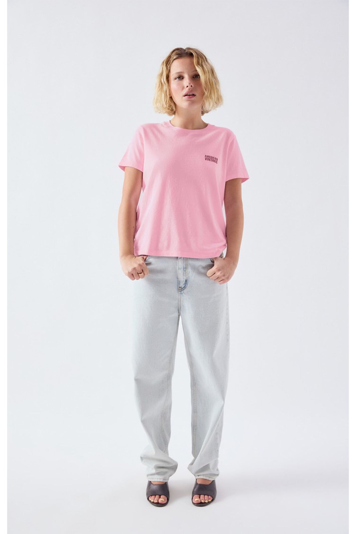 Model wearing the American Vintage Ykobow Cotton T-Shirt – Bon Bon in soft pink paired with light denim jeans and black sandals, shop American Vintage at Dotique.