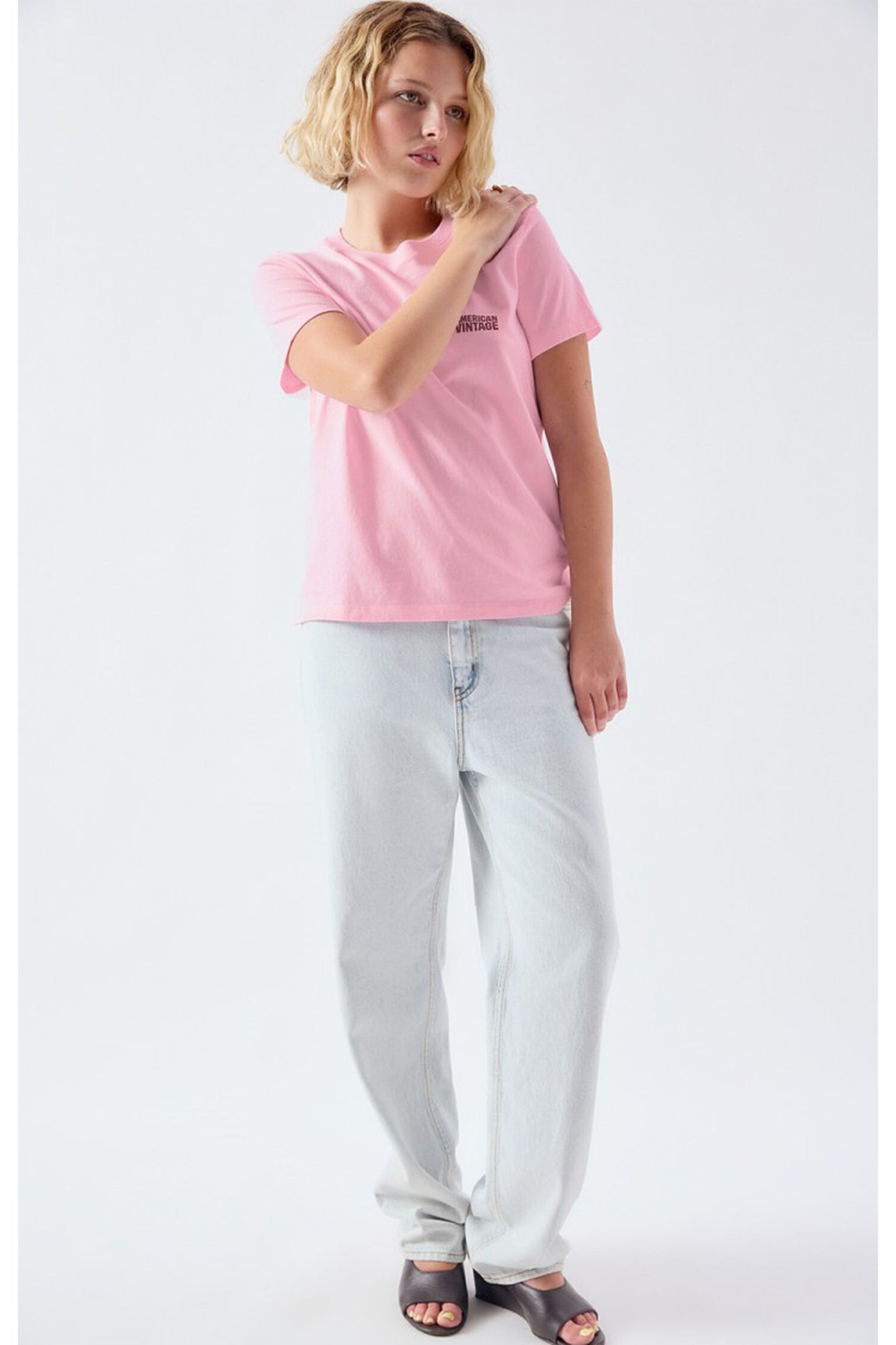 Model wearing the American Vintage Ykobow Cotton T-Shirt – Bon Bon in soft pink paired with light washed jeans and black open-toe heels, shop American Vintage at Dotique.