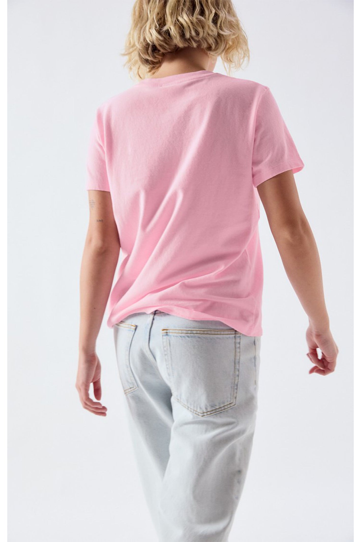Rear view of a person wearing the American Vintage Ykobow Cotton T-Shirt – Bon Bon in pink paired with light jeans, shop American Vintage at Dotique.