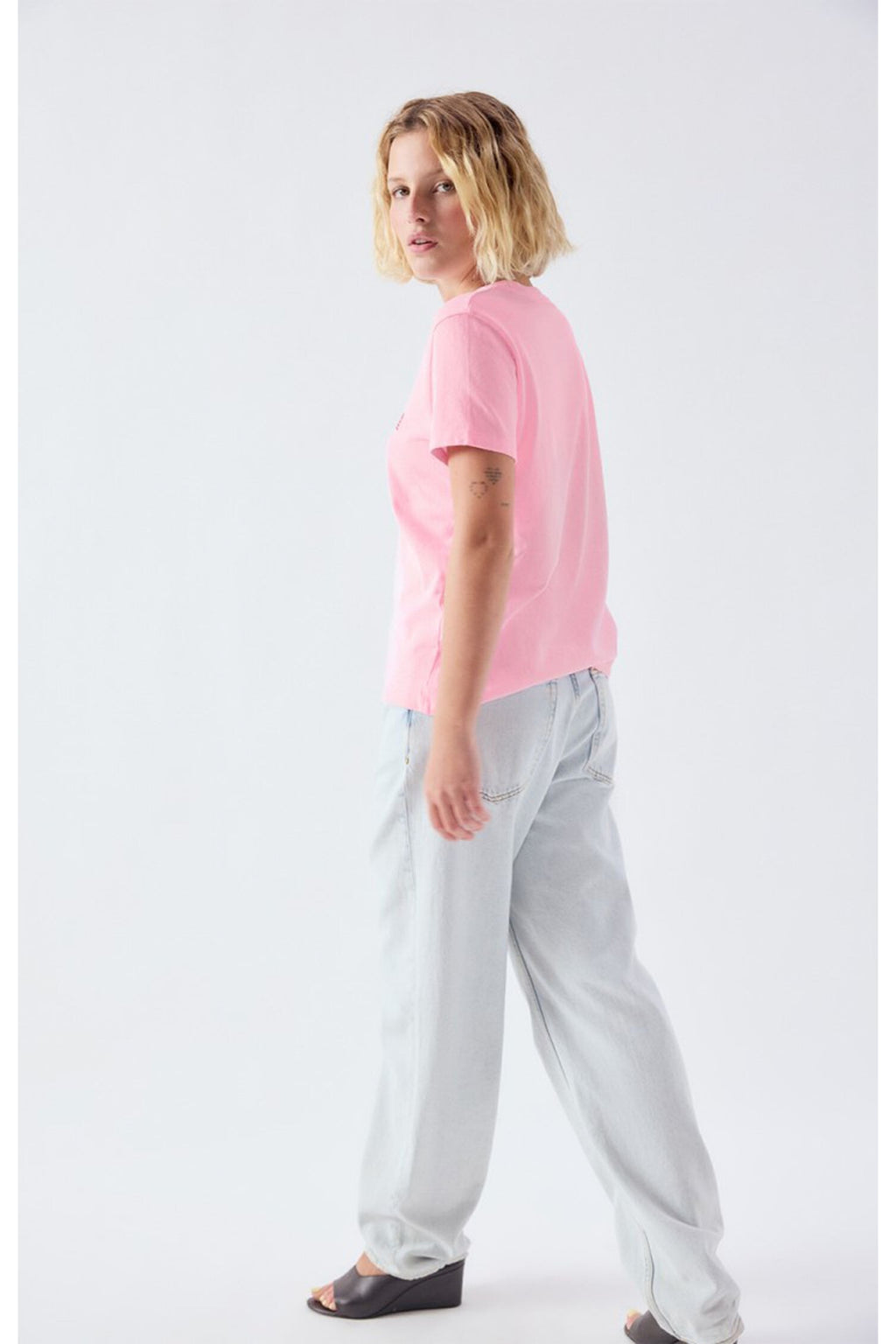 Woman modeling the American Vintage Ykobow Cotton T-Shirt – Bon Bon in pink paired with light denim jeans and black wedge sandals, shop American Vintage at Dotique.