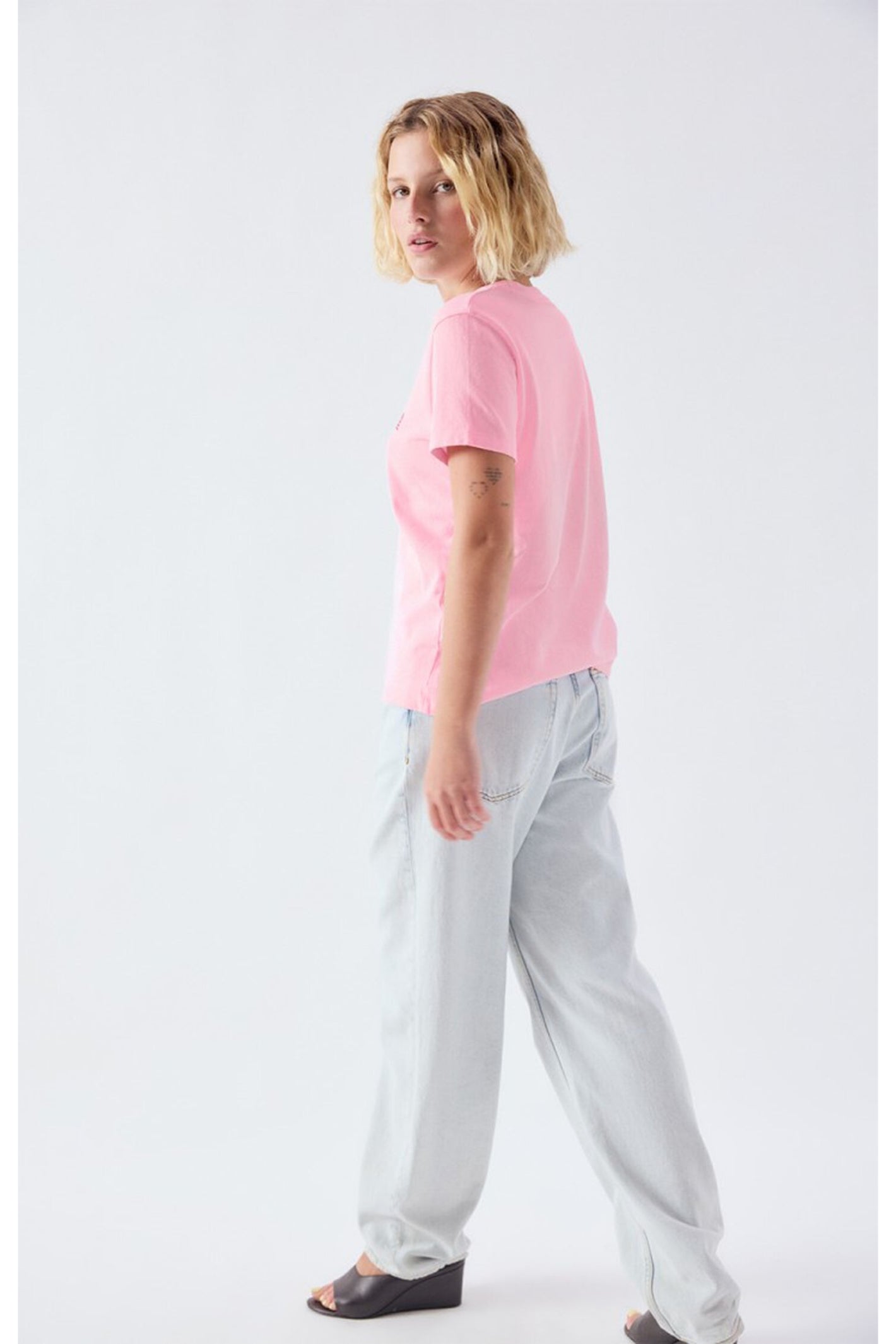 Woman modeling the American Vintage Ykobow Cotton T-Shirt – Bon Bon in pink paired with light denim jeans and black wedge sandals, shop American Vintage at Dotique.