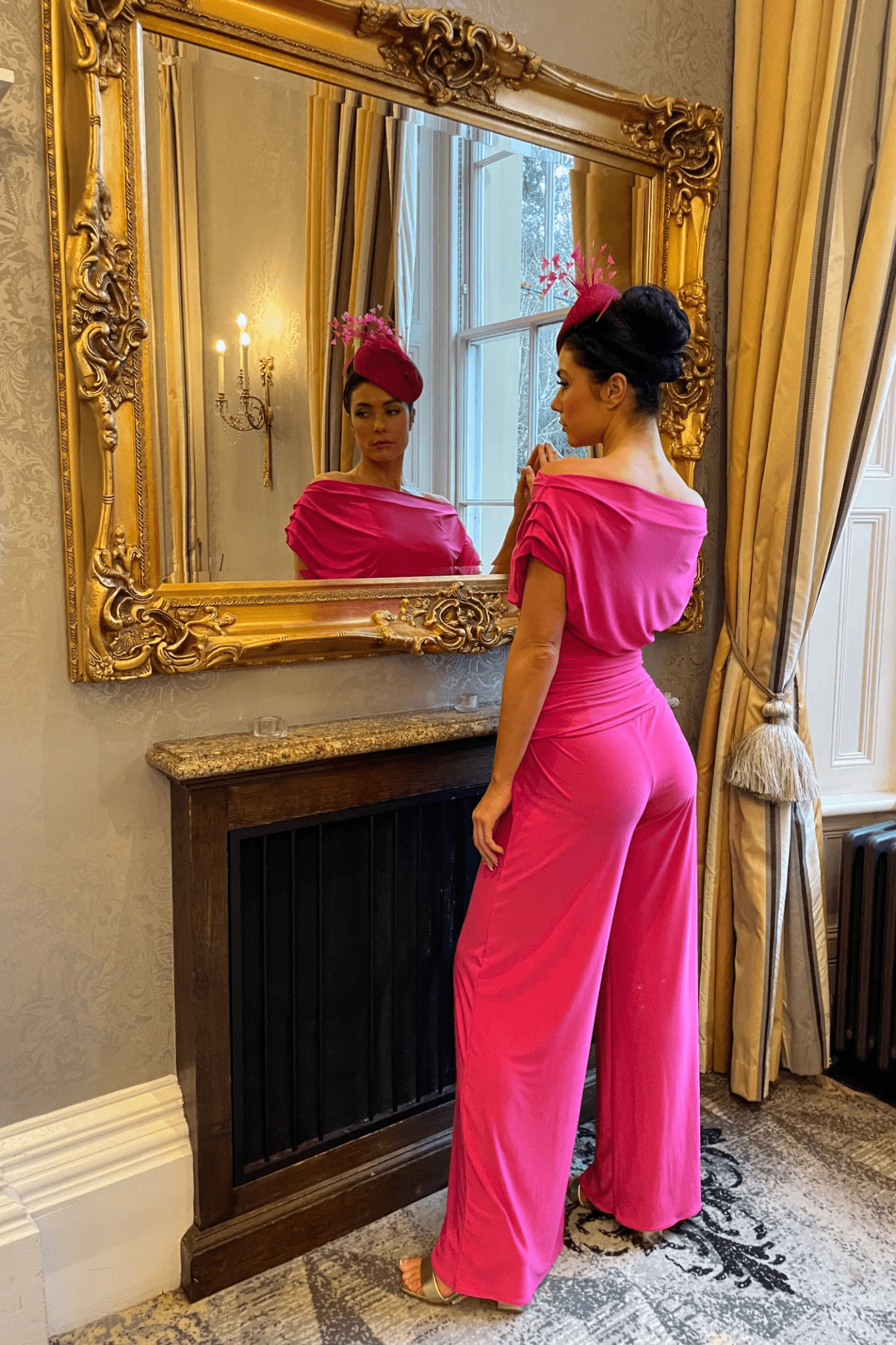 Woman wearing ATOM LABEL Carbon Jumpsuit in Hot Pink by ATOM LABEL, standing by mirror, shop ATOM LABEL at Dotique.