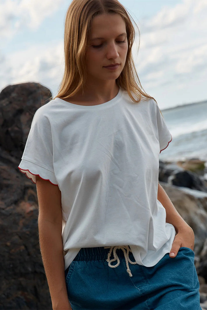 Model wearing Betty Basics Sloane T-Shirt in white with red scallop trim, outdoor styling