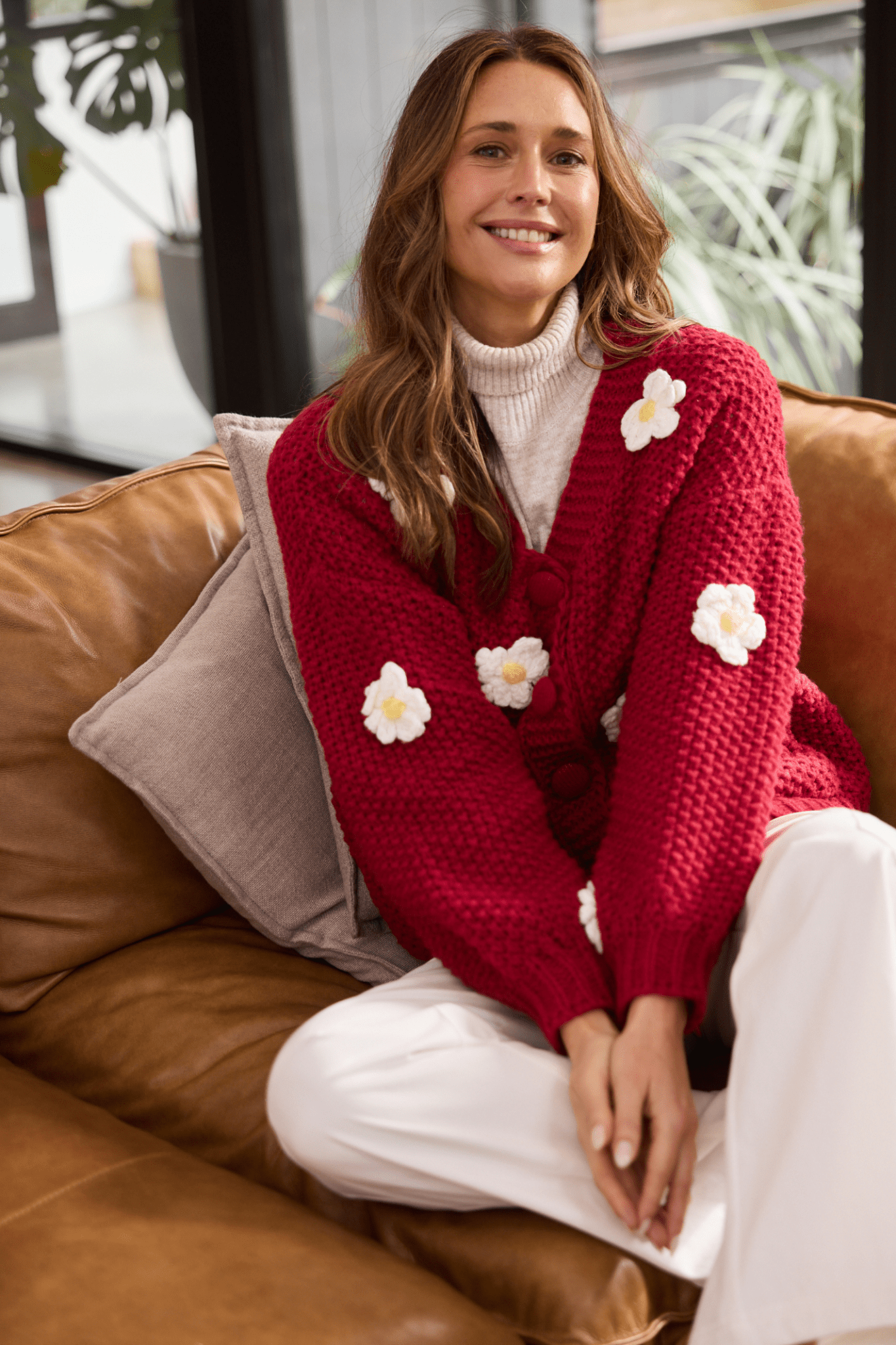 Woman wearing a red sweater with white flower patterns, sitting on a brown couch.