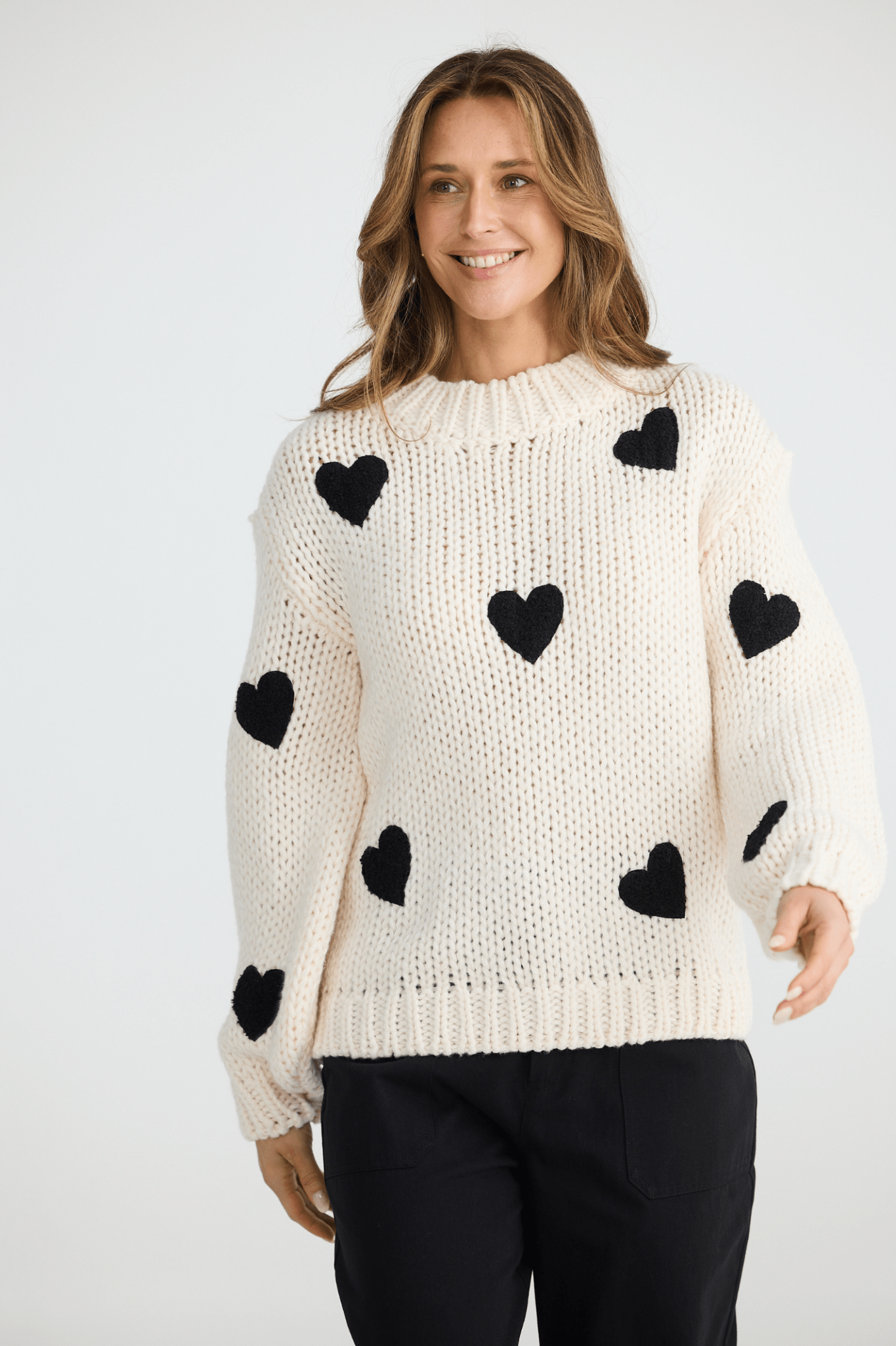 Woman wearing a cream sweater with black heart patterns on a white background