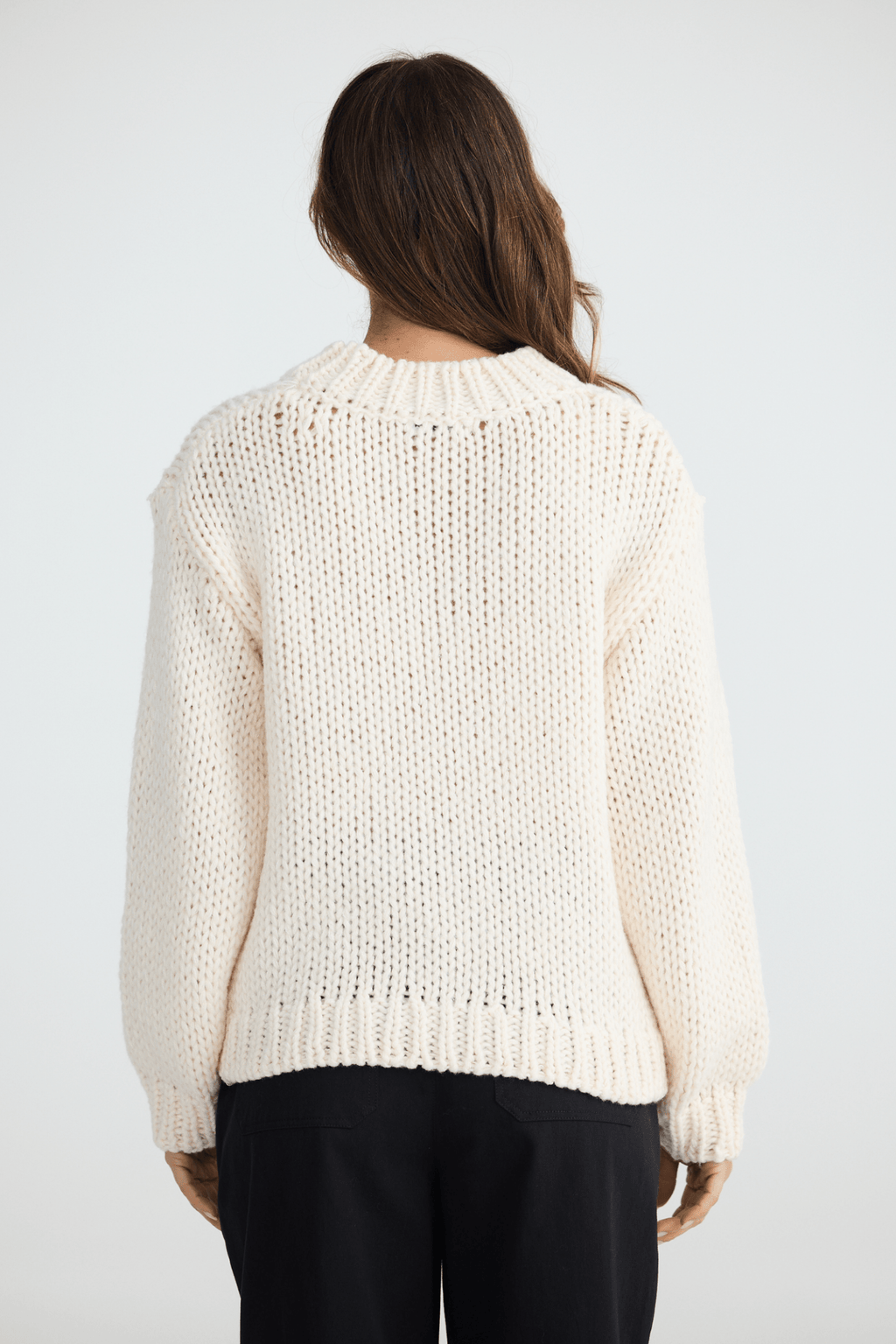 Person wearing a cream knitted sweater on a white background