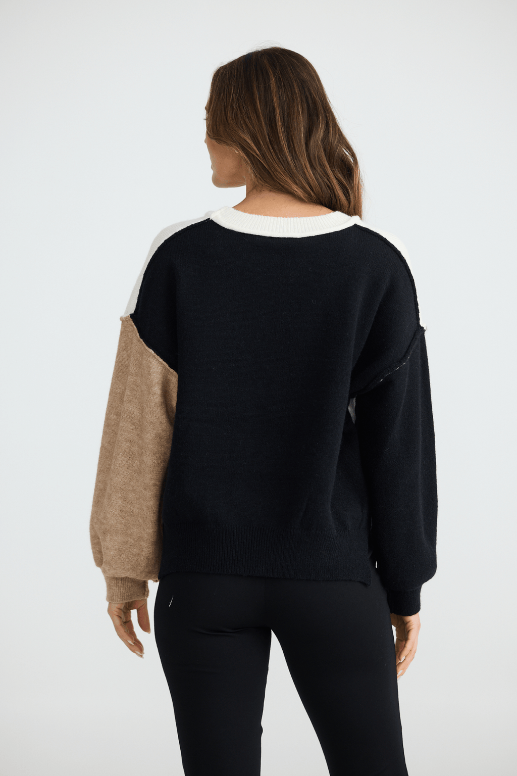 Person wearing a black sweater with beige sleeves on a white background