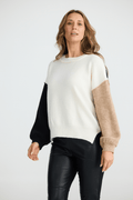 Woman wearing a color-blocked sweater with black, beige, and white sections on a white background