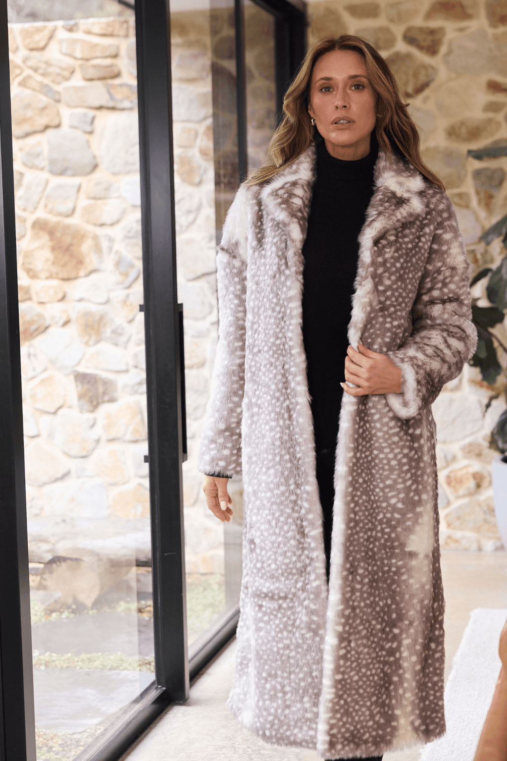 Woman wearing a long, patterned coat standing in front of a stone wall.