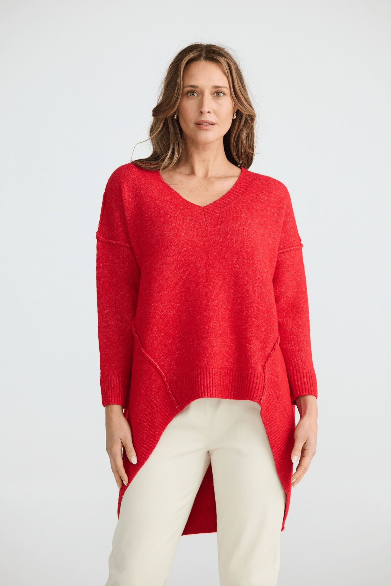 Woman wearing a red sweater and white pants on a light gray background