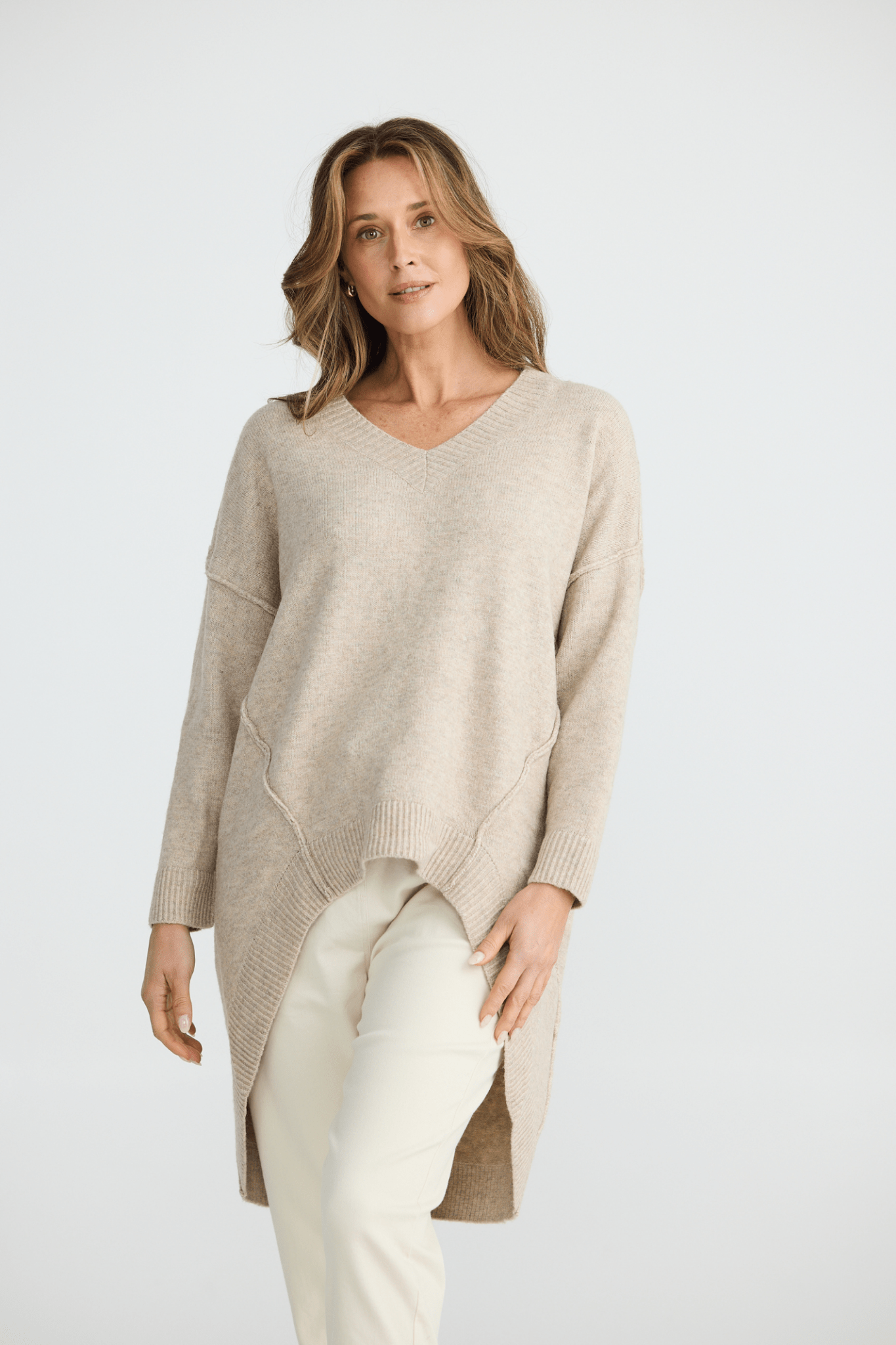 Woman wearing a beige sweater and white pants on a white background