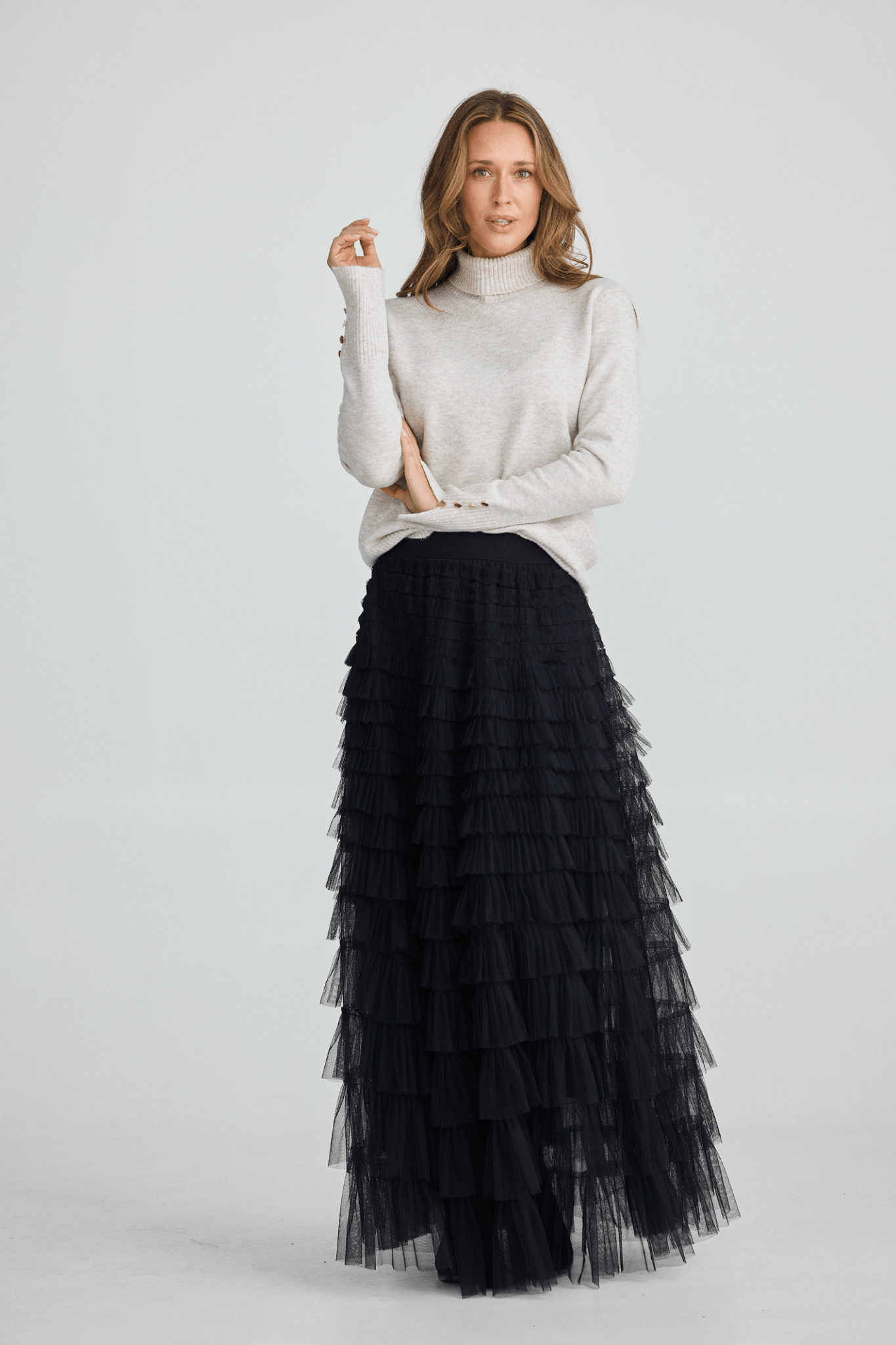 Woman wearing a white turtleneck sweater and black tiered skirt on a light gray background