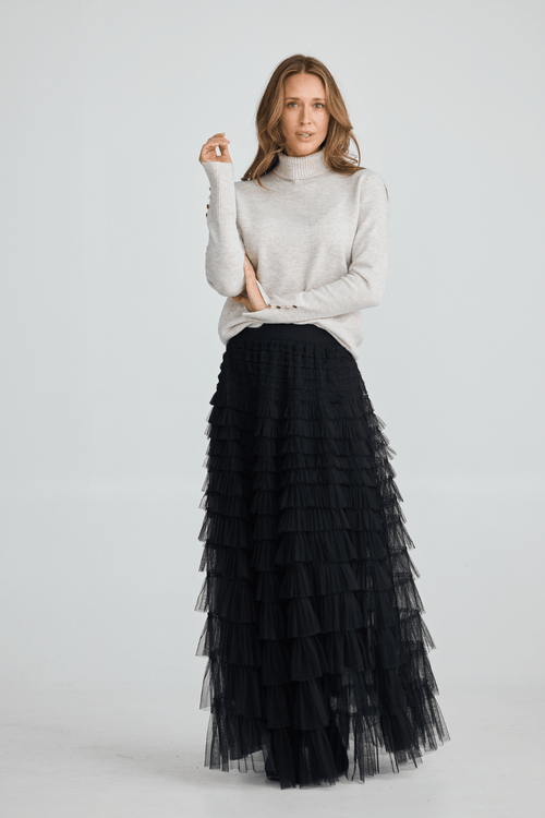 Woman wearing a white turtleneck sweater and black tiered skirt on a light gray background