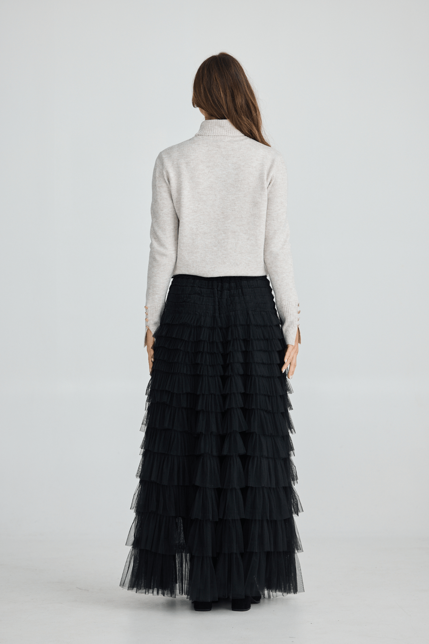Woman wearing a white turtleneck sweater and black tiered skirt on a white background