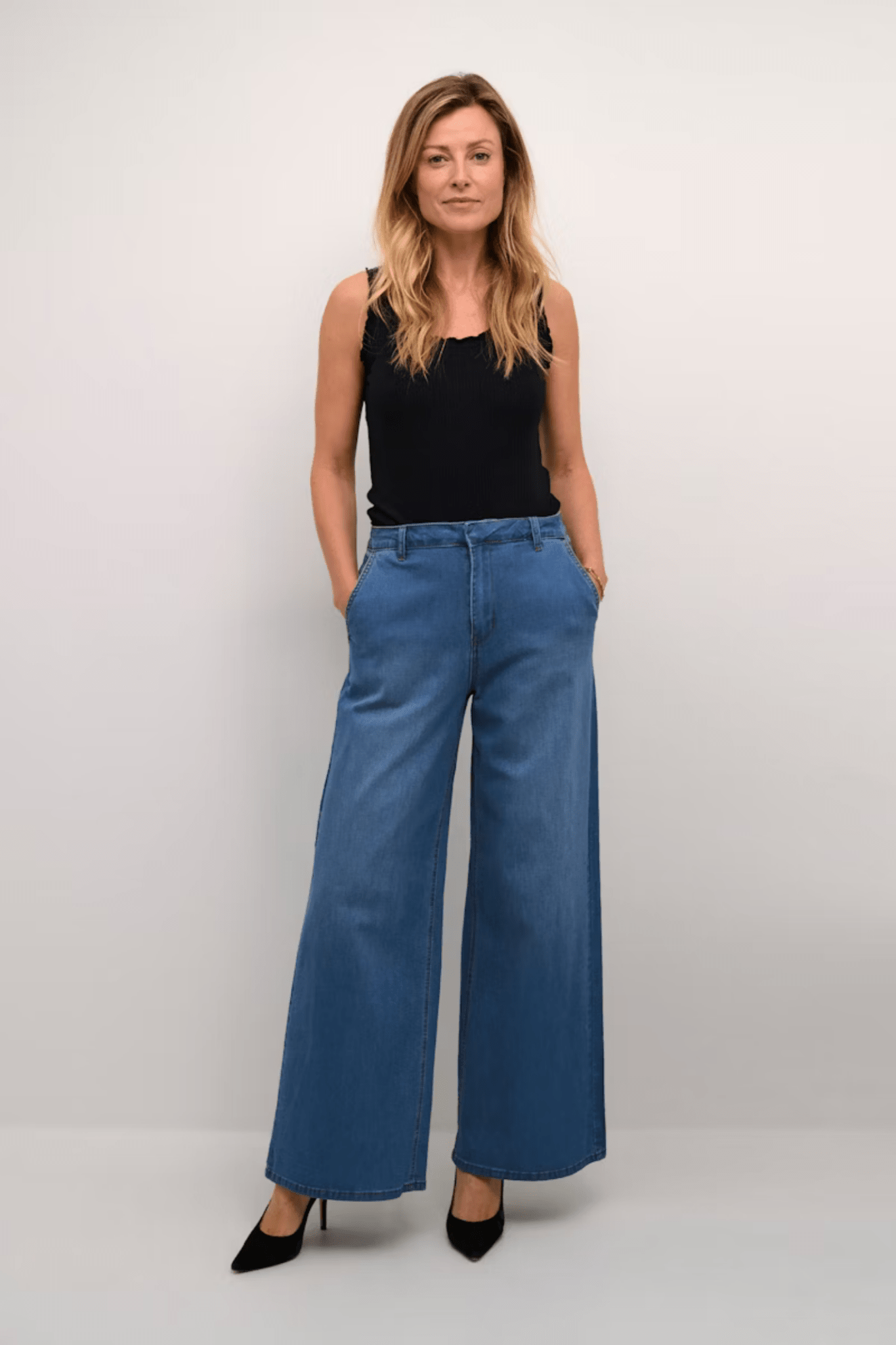 Woman wearing blue wide-leg jeans and a black top on a plain background