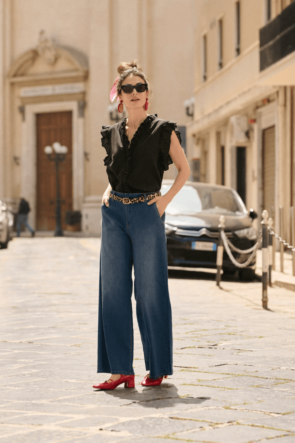 Woman in black sleeveless top and blue wide-leg pants standing on a city street.