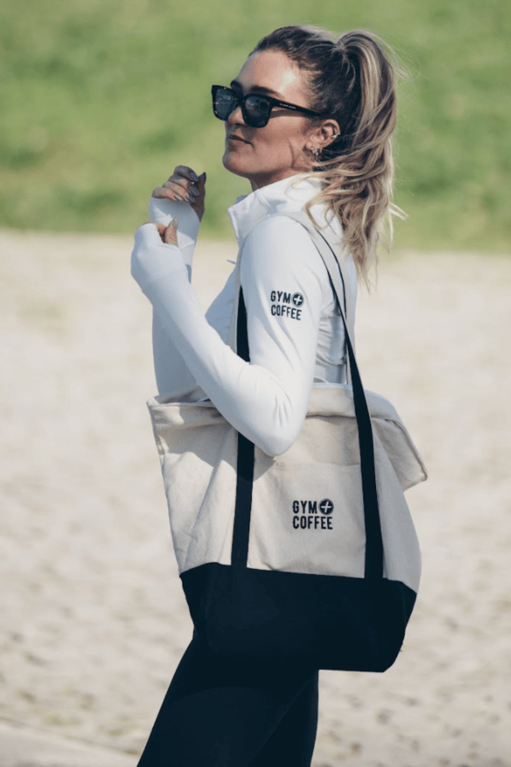Woman wearing Gym+Coffee Relentless Full Zip Jacket in Ultra White with tote bag, shop Gym+Coffee at Dotique for activewear styles