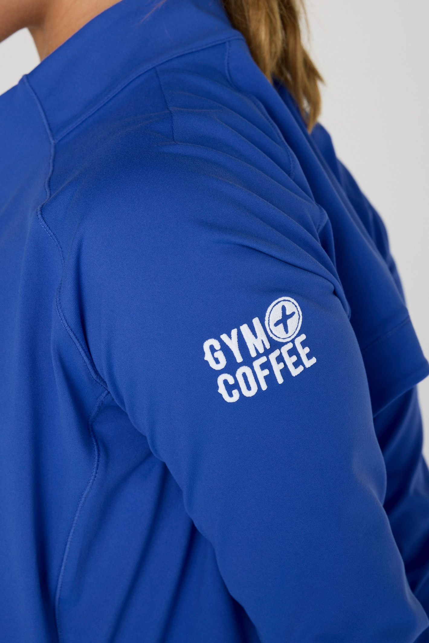 Close-up of sleeve detail featuring Gym+Coffee logo on Gym+Coffee Relentless Full Zip Tidal Blue, shop at Dotique.
