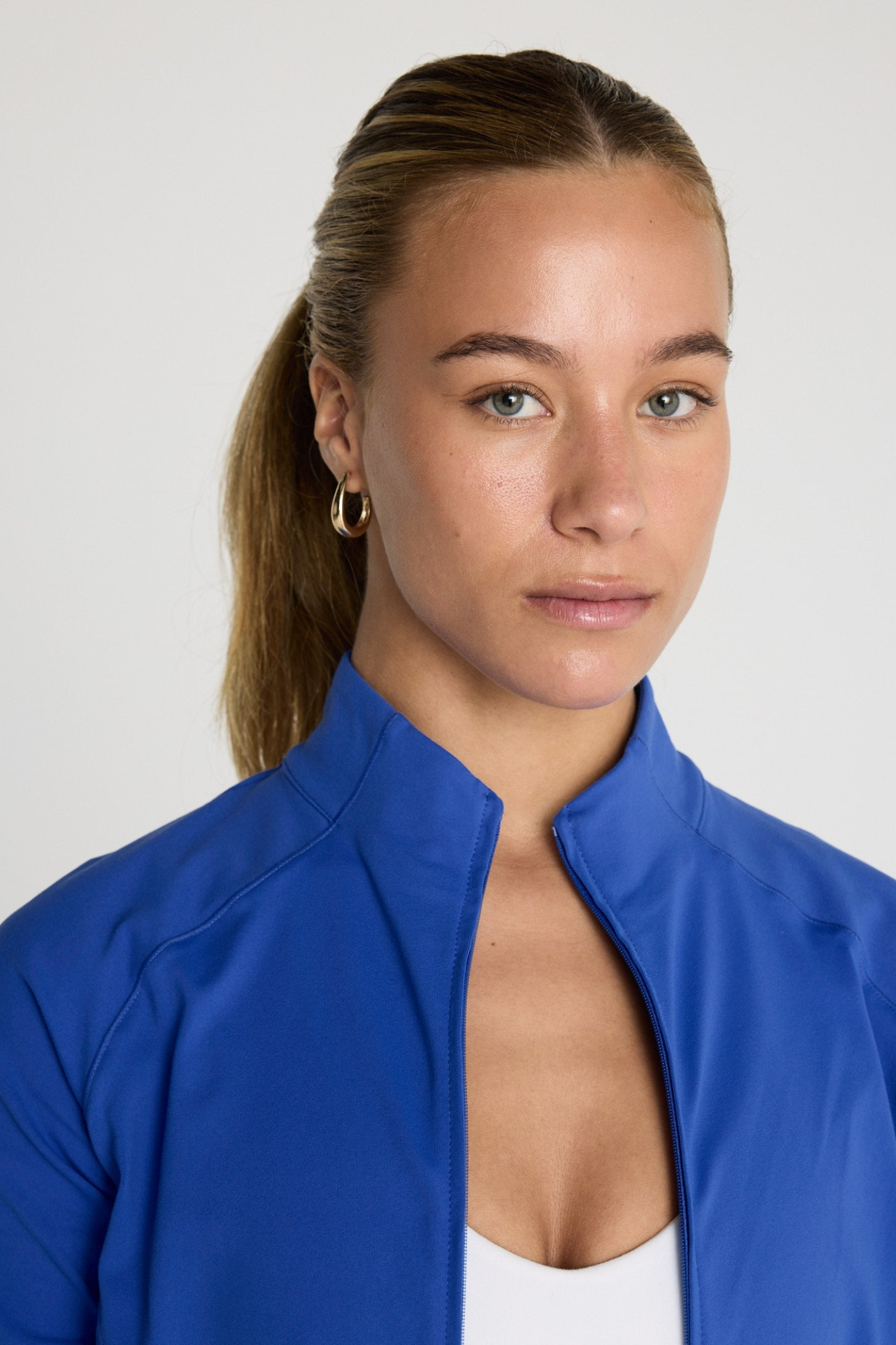 Close-up of a woman wearing Gym+Coffee Relentless Full Zip Tidal Blue jacket, shop Gym+Coffee at Dotique.