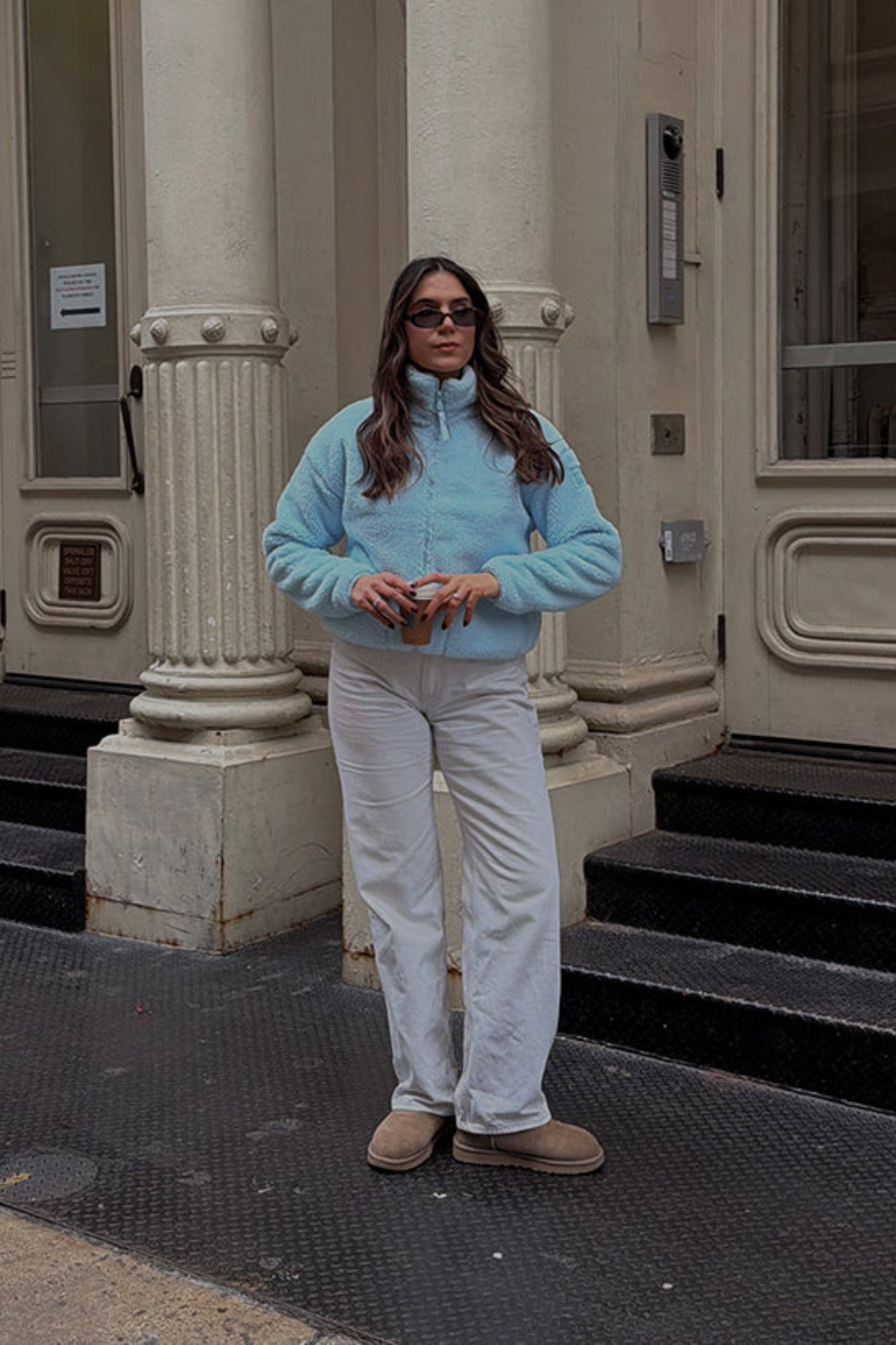 Woman wearing Gym+Coffee Industry Fleece High Collar Jacket in Baby Blue holding cup outside shop Shop Gym+Coffee at Dotique