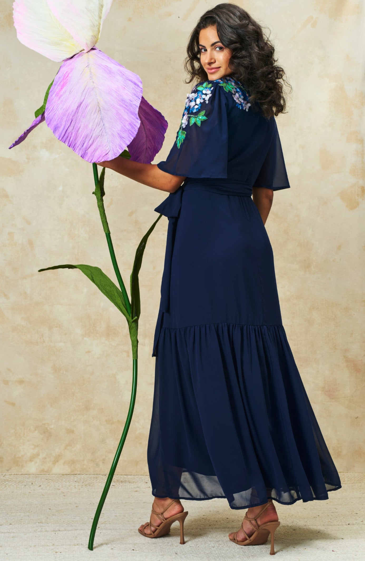 Model wearing Hope & Ivy Sadie Flutter Sleeve Blue Maxi Dress with Tie Waist holding giant flower Shop Hope and Ivy at Dotique