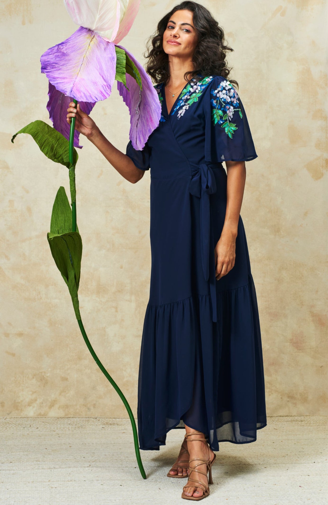 Woman wearing Hope & Ivy Sadie Flutter Sleeve Blue Maxi Dress with Tie Waist holding large flower Shop Hope and Ivy at Dotique