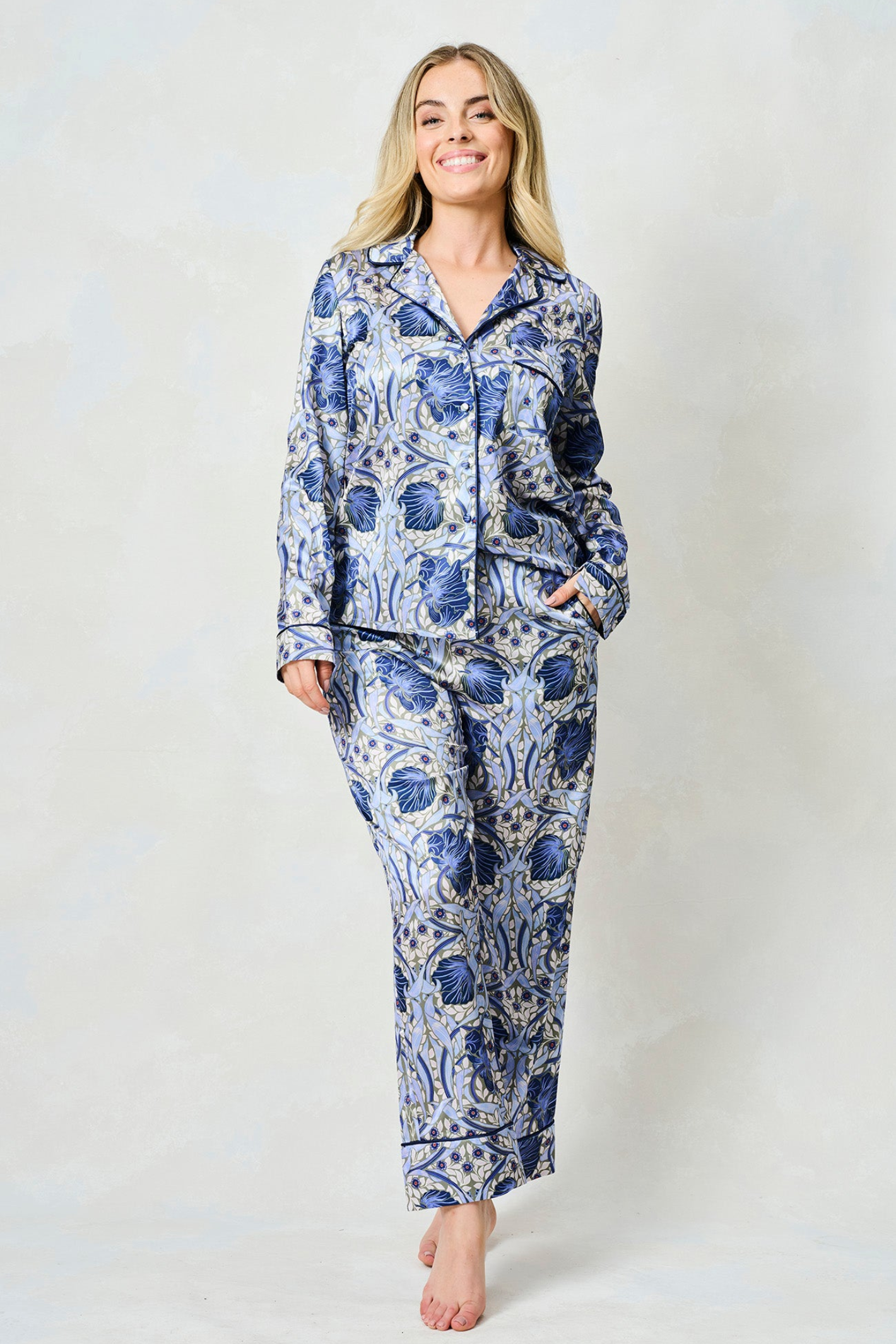 Woman wearing blue and white floral patterned satin pyjama set with long sleeves and wide-leg trousers against light background