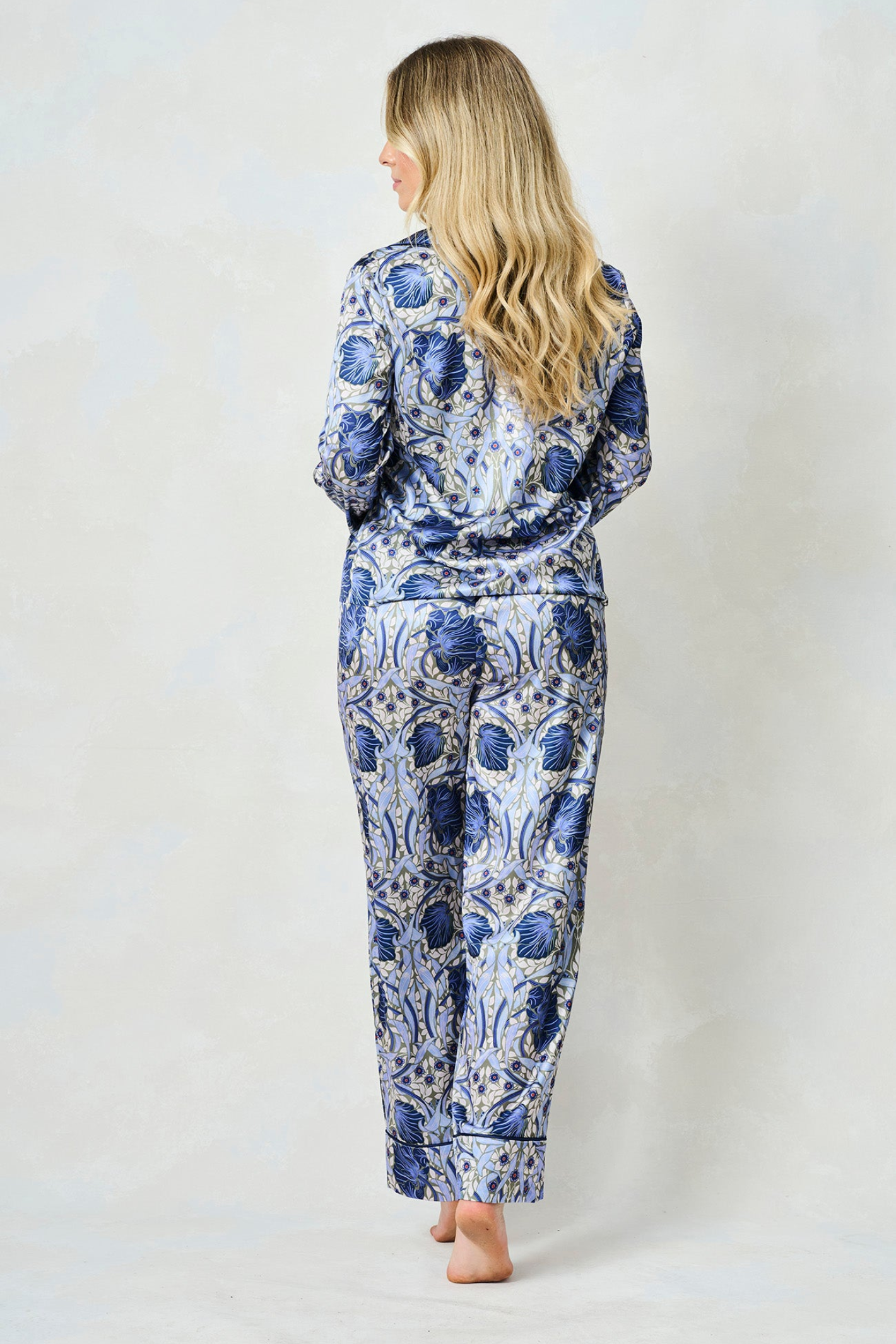Woman seen from back wearing blue and white floral patterned satin pyjama set against neutral background