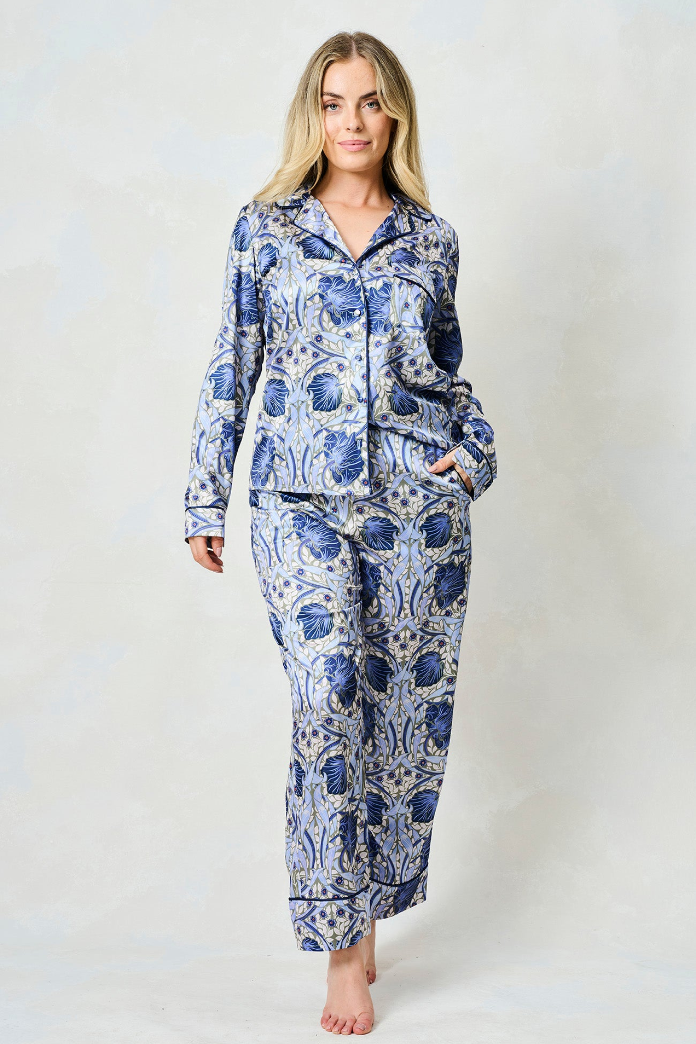 Woman wearing blue and beige floral patterned satin pyjama set with long sleeves and straight-leg trousers on light background