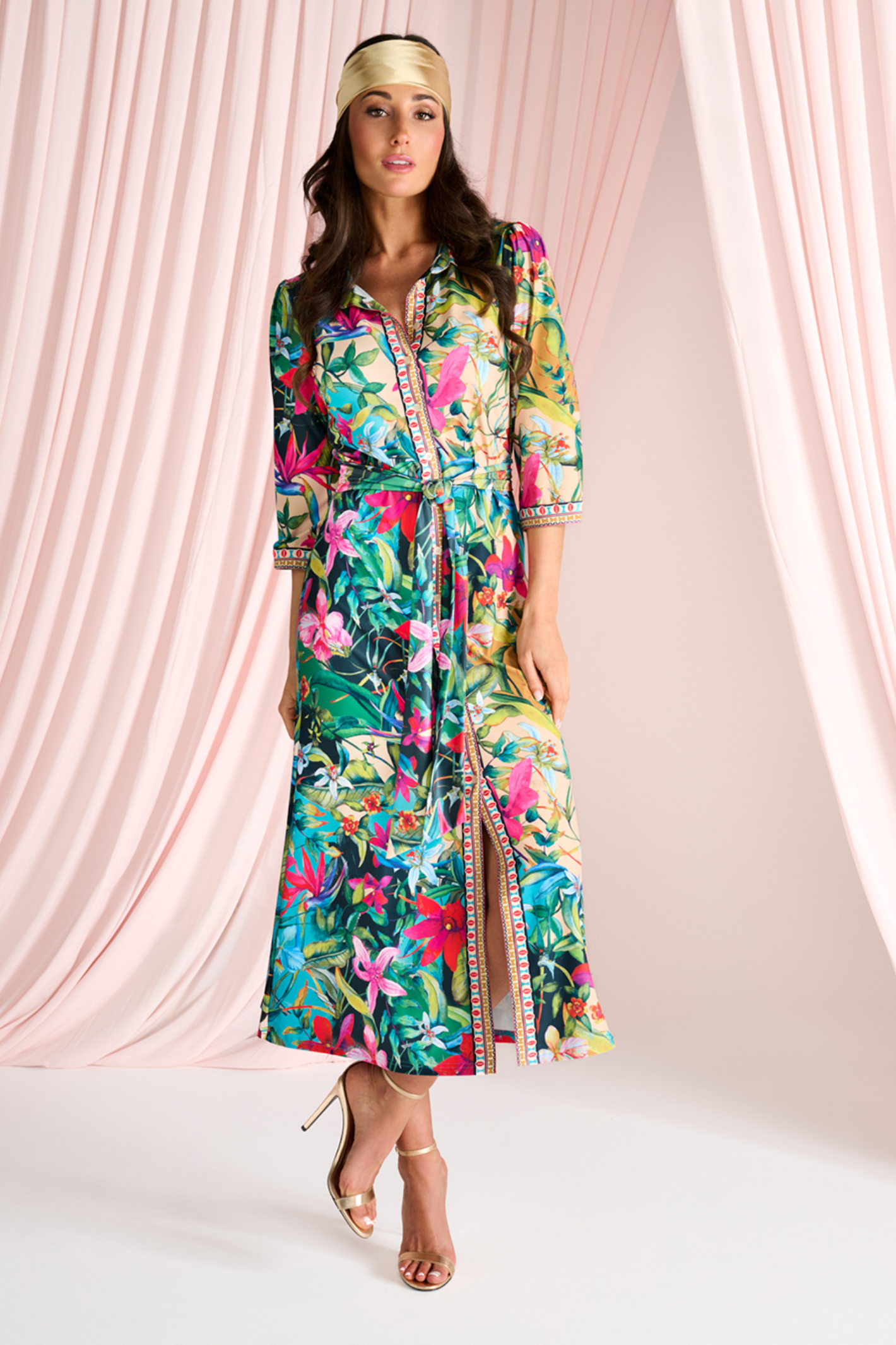 Model wearing colorful tropical print button-up maxi dress with three-quarter sleeves and belted waist on neutral background