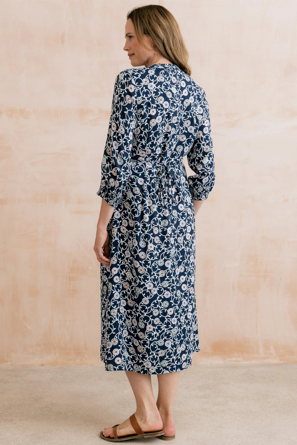 Model seen from behind wearing Lily & Me LM26022 Leoni Dress Sea Holly Navy with floral print and tie waist by Lily & me. Shop Lily & me at Dotique.