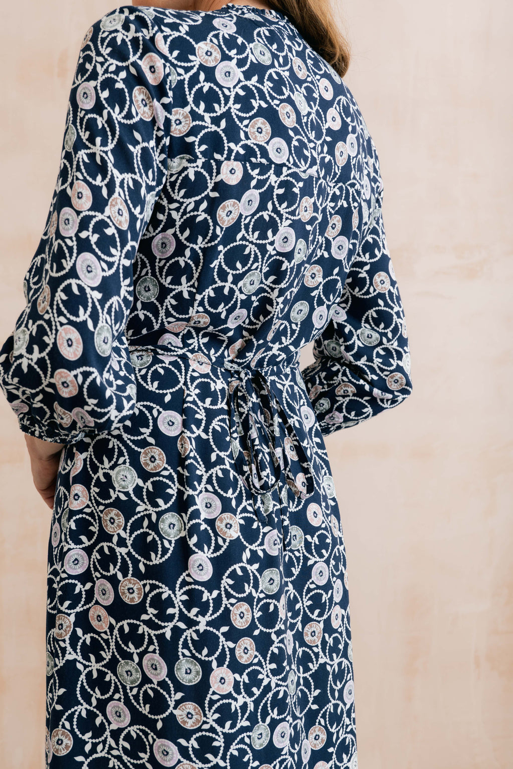 Model wearing Lily & Me LM26022 Leoni Dress Sea Holly Navy with intricate floral pattern and waist tie by Lily & me. Shop Lily & me at Dotique.
