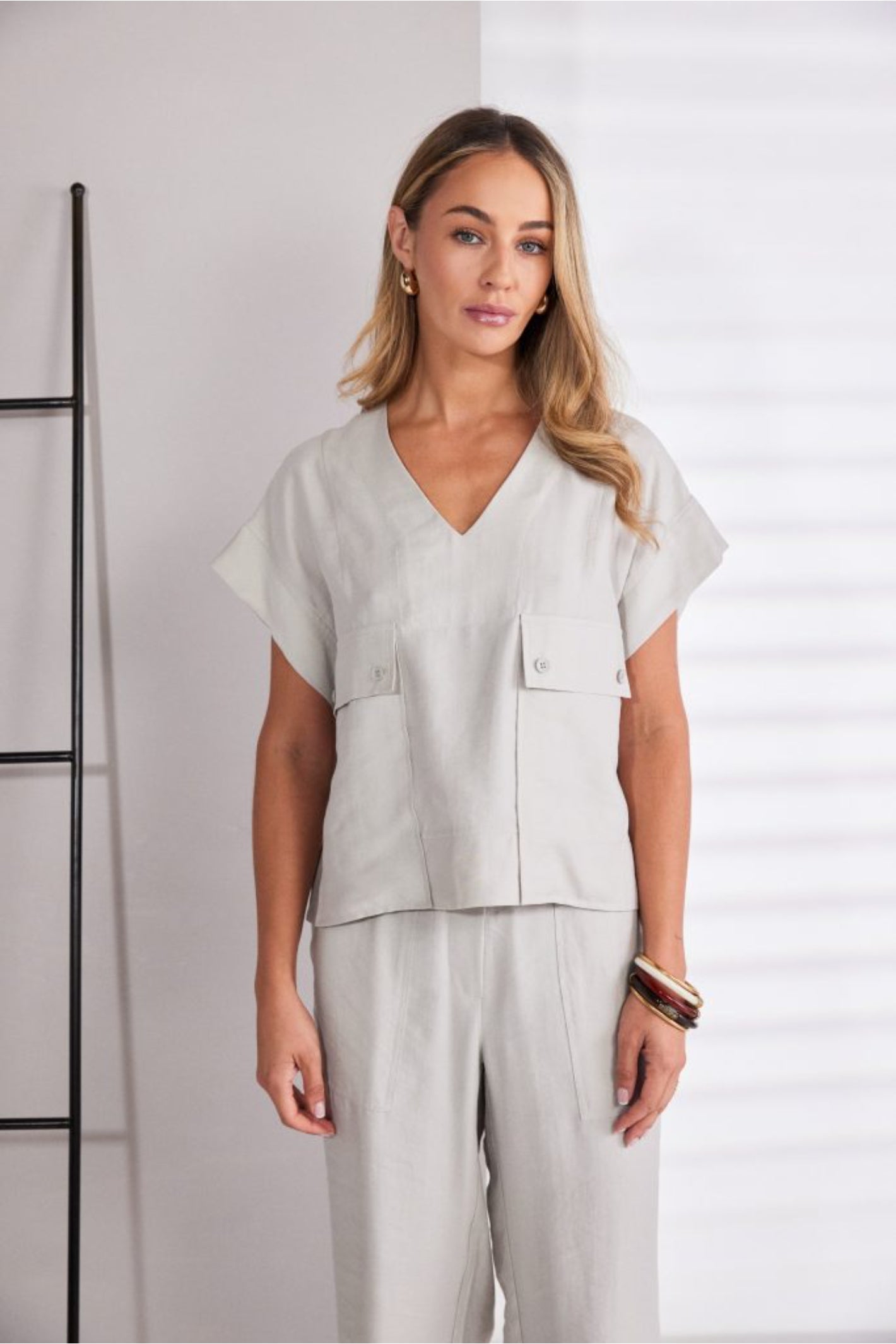 Model wearing Naya NPA26220 Patch Pocket Vee Neck Top With Button Detail Ash by Naya, styled with matching trousers. Shop Naya at Dotique.