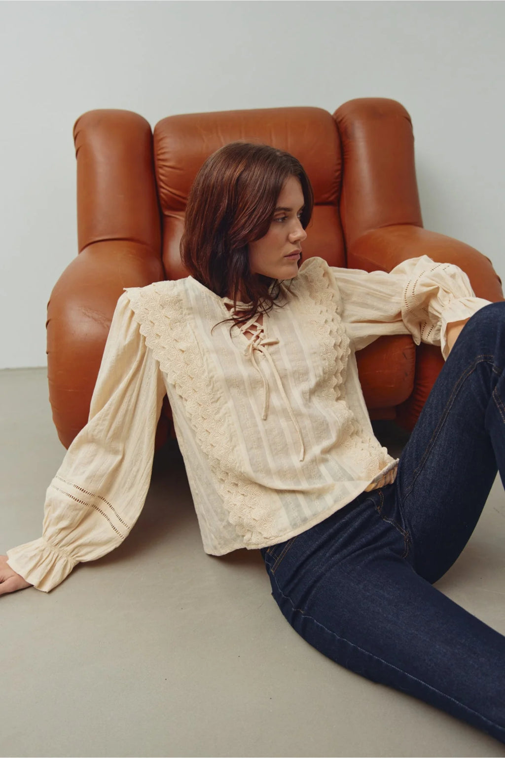 Woman wearing Noella 15320002 N-Maliyah Blouse Ivory by Noella sitting near brown armchair Shop Noella at Dotique