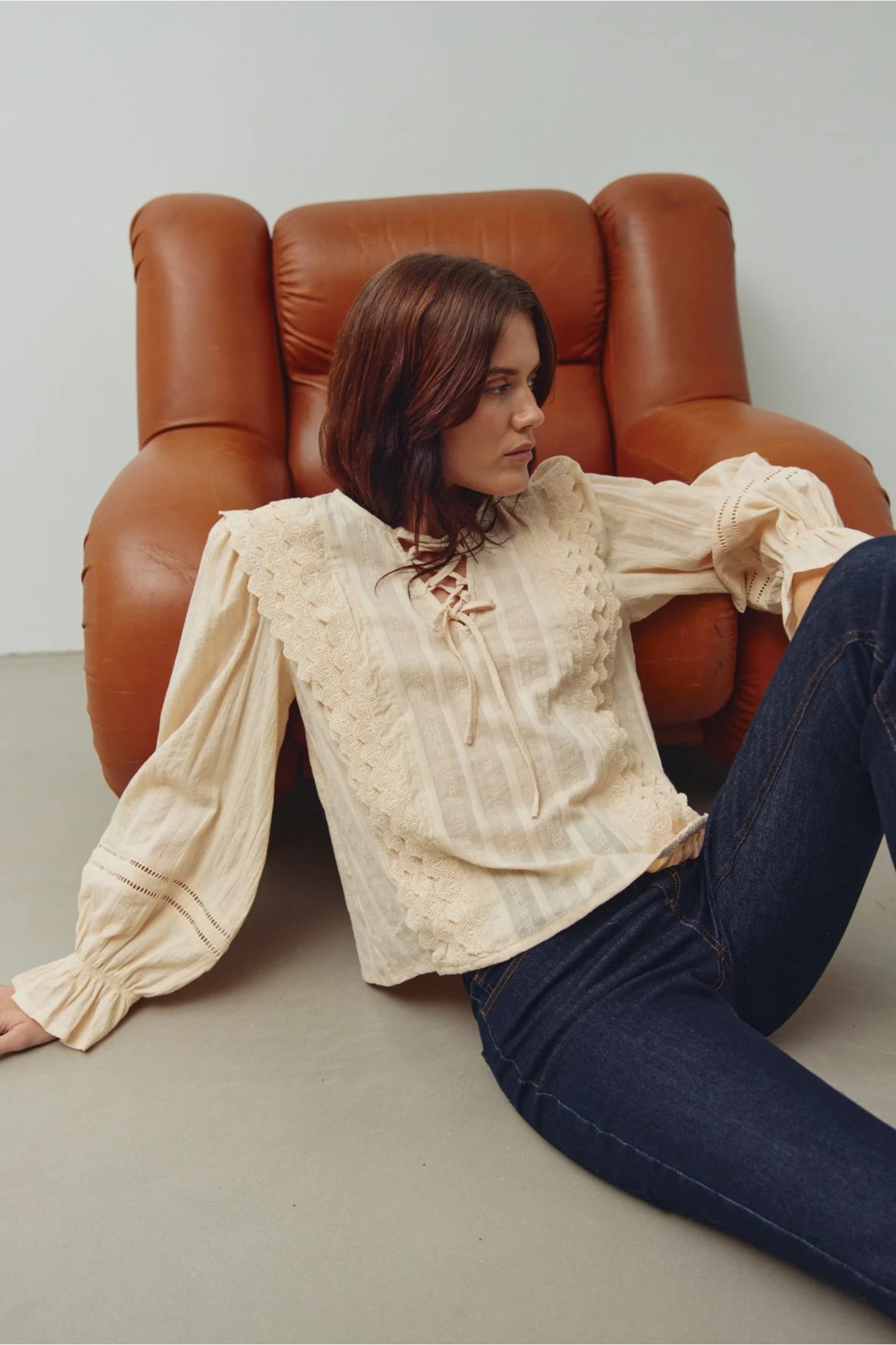 Woman wearing Noella 15320002 N-Maliyah Blouse Ivory by Noella sitting near brown armchair Shop Noella at Dotique