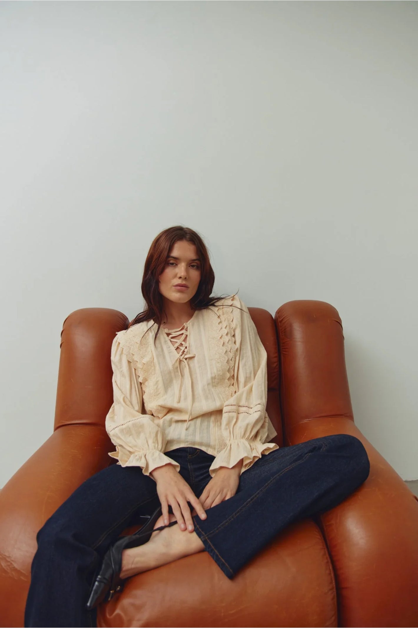 Model wearing Noella 15320002 N-Maliyah Blouse Ivory sitting on a brown chair, shop Noella at Dotique