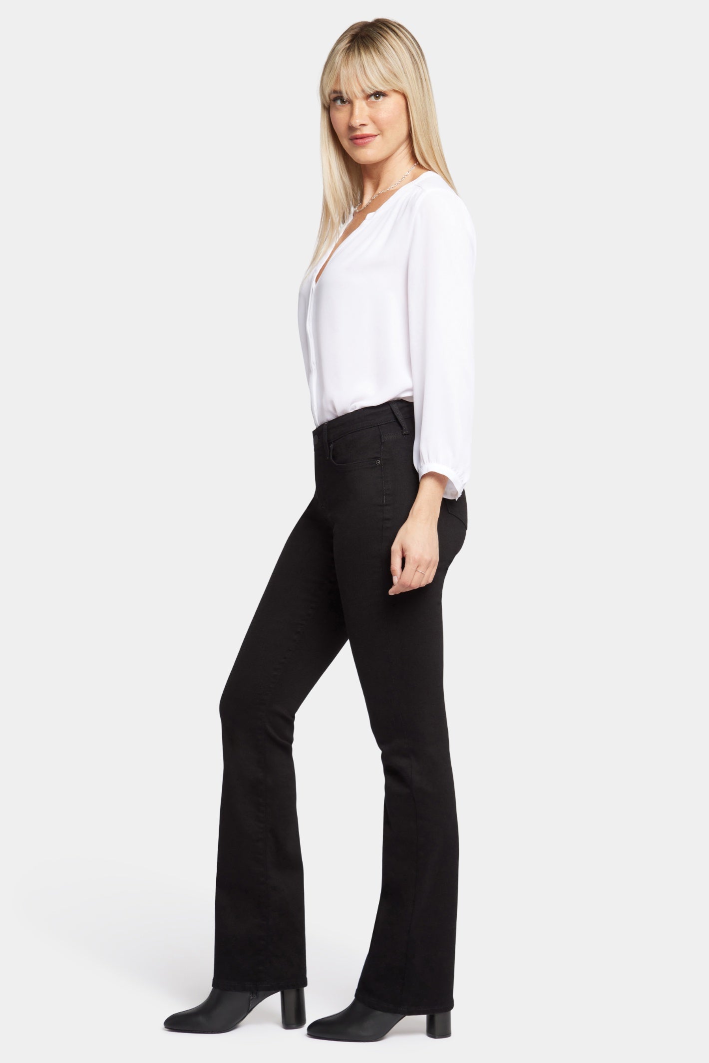 Woman wearing NYDJ Barbara Bootcut Black Jeans 30” styled with a white blouse and black boots shop NYDJ at Dotique