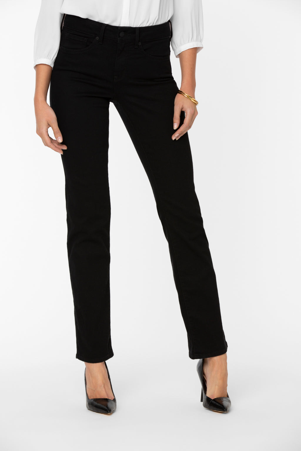 Woman wearing NYDJ Barbara Bootcut Black Jeans 30” styled with black heels and white blouse Shop NYDJ at Dotique