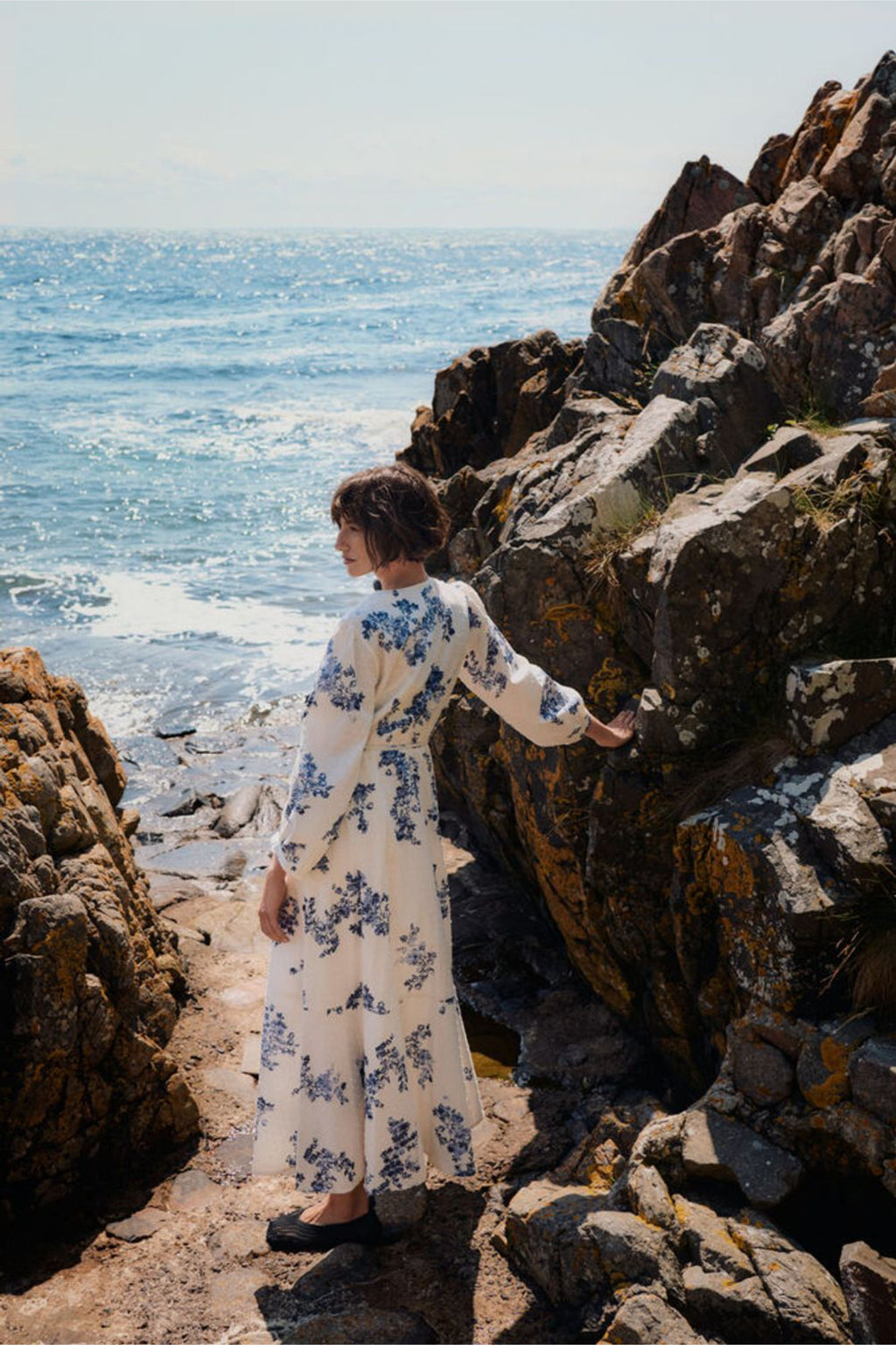Woman wearing Part Two 30310448 AlyaPW Blue Shadow Flower Print Dress by Part Two standing by rocky shore Shop Part Two at Dotique