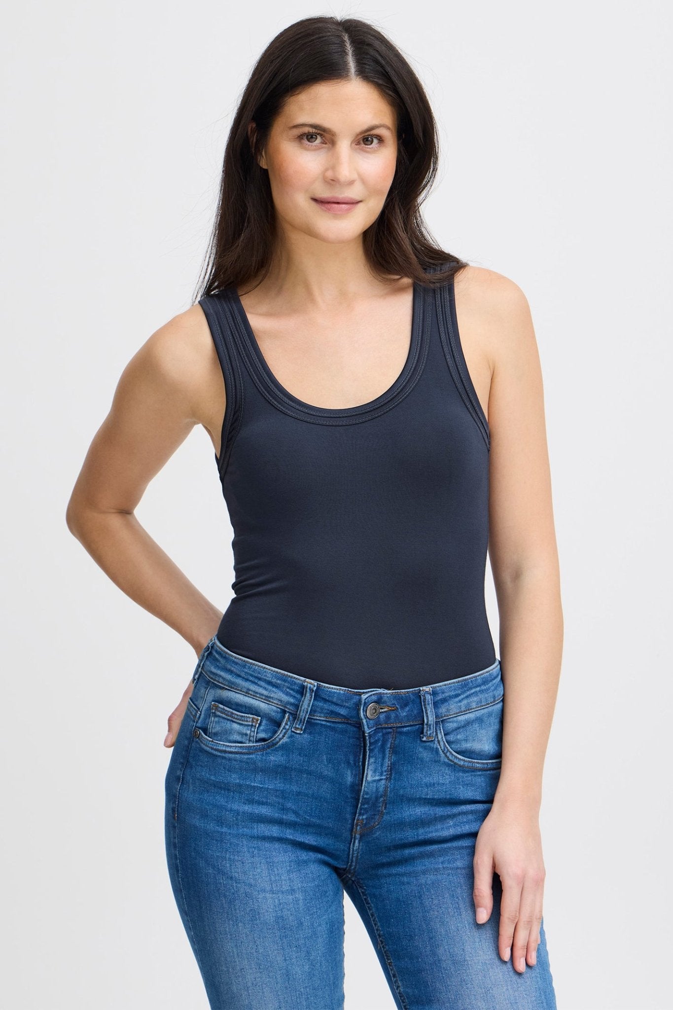 Woman wearing a navy tank top and blue jeans on a white background